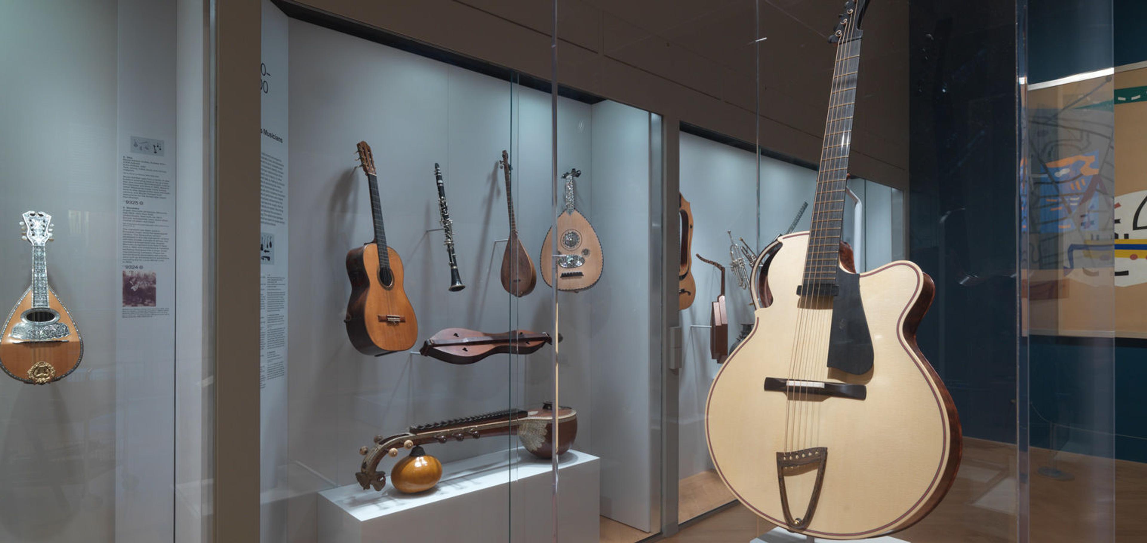 Picture of one of the musical instrument galleries at The Met, with several instruments such as guitars and mandolins in glass cases.