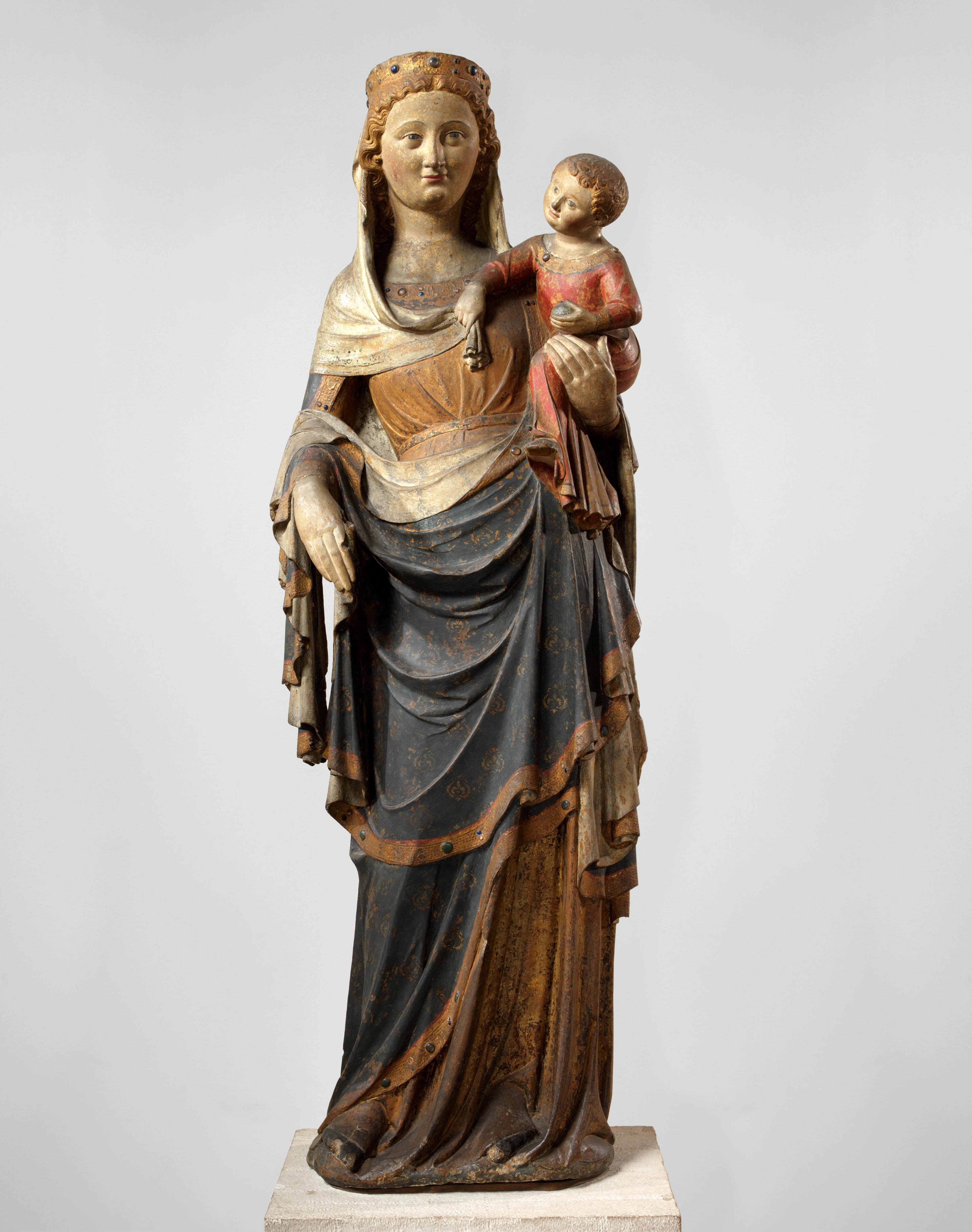 Tall sculpture depicting Mary with layered robes, carrying a small child in her left arm.