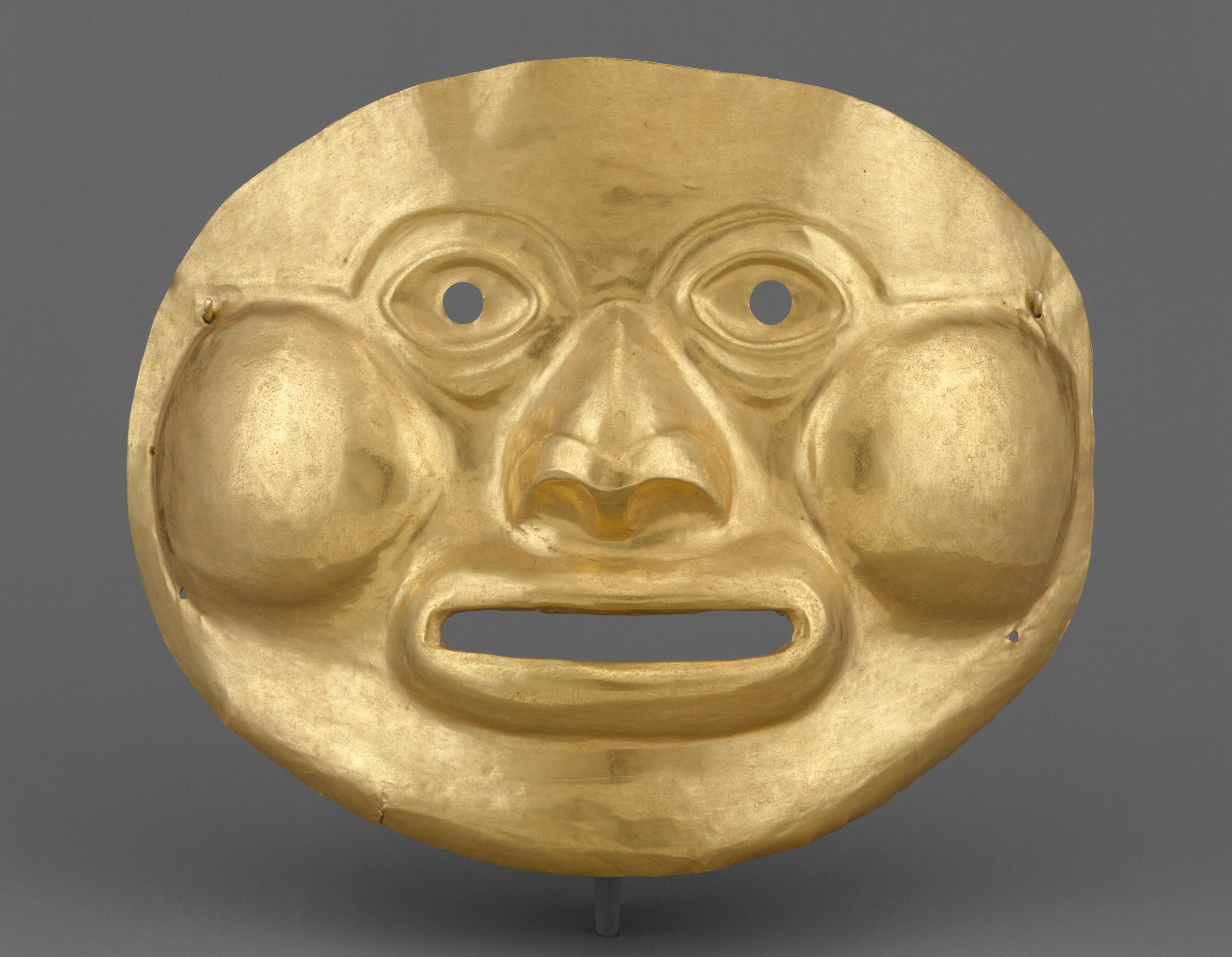 A gold mask with a smooth, symmetrical form and prominent cheek contours, shown against a gray background.