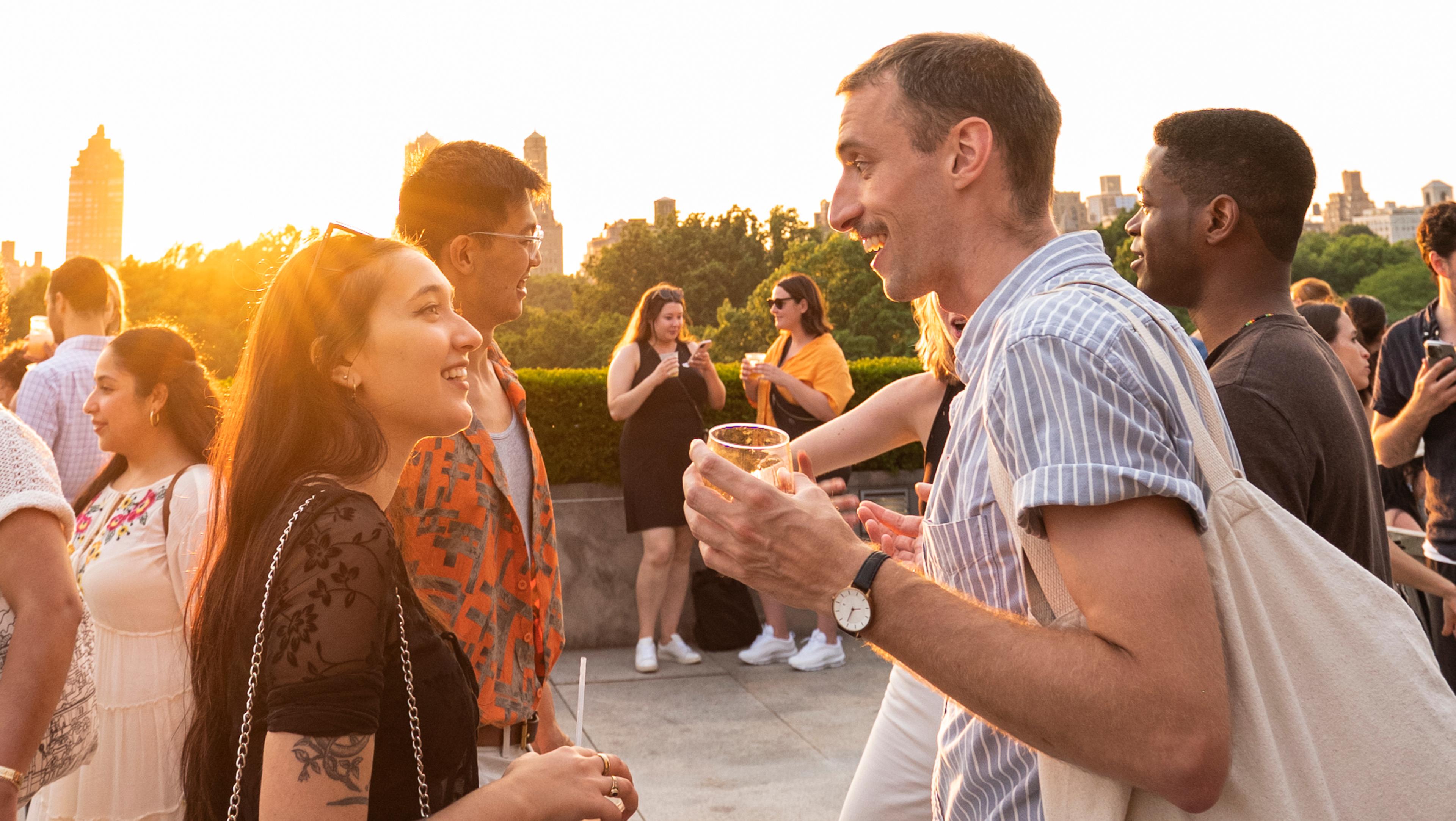 A group of people with drinks on The Met's Roof Garden during sunset