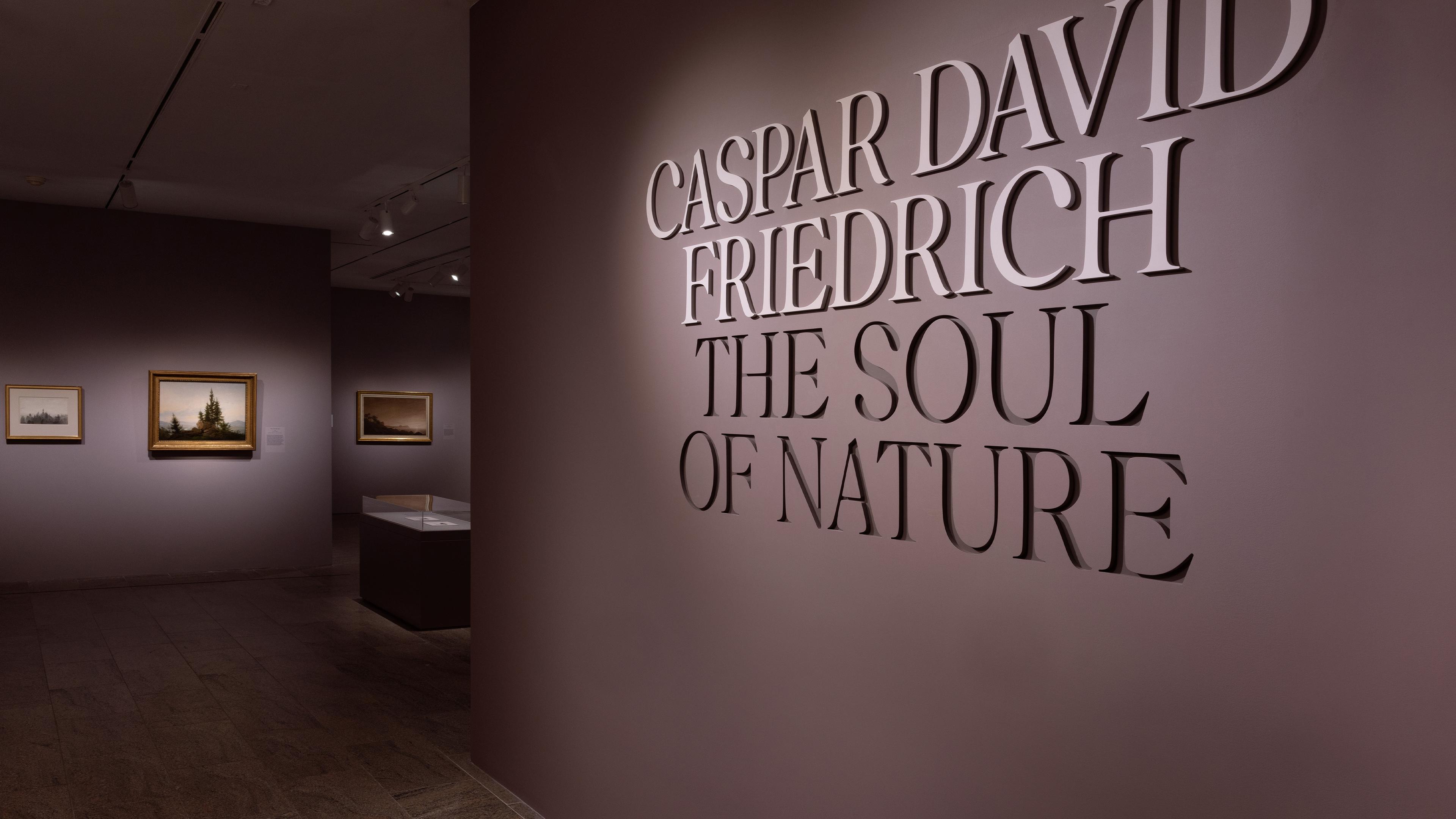 Exhibition entrance with "Caspar David Friedrich: The Soul of Nature" on a wall. Dimly lit room with framed landscape paintings displayed.