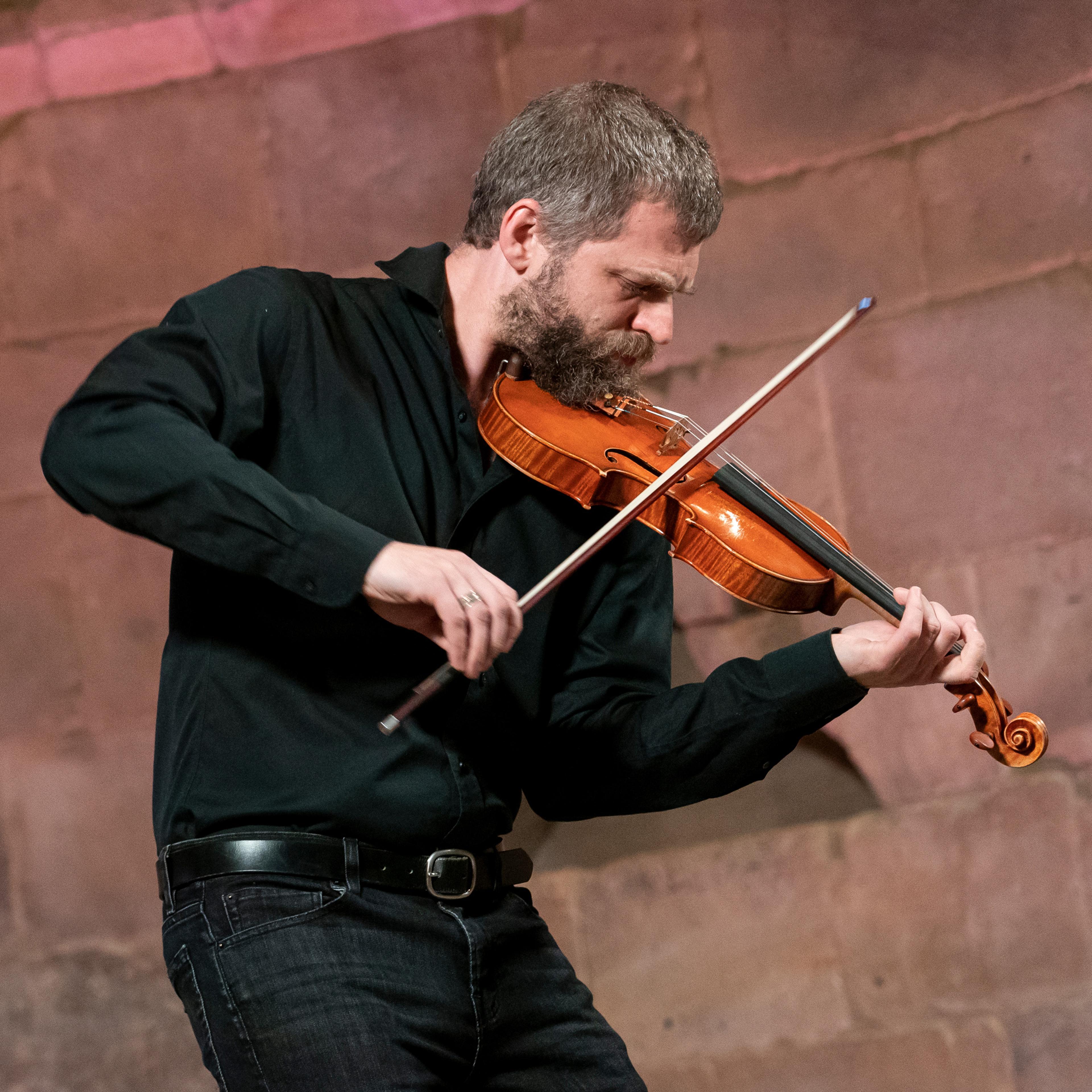 Johnny Gandelsman leans into a violin in performance at The Met Cloisters. He wears a black shirt.