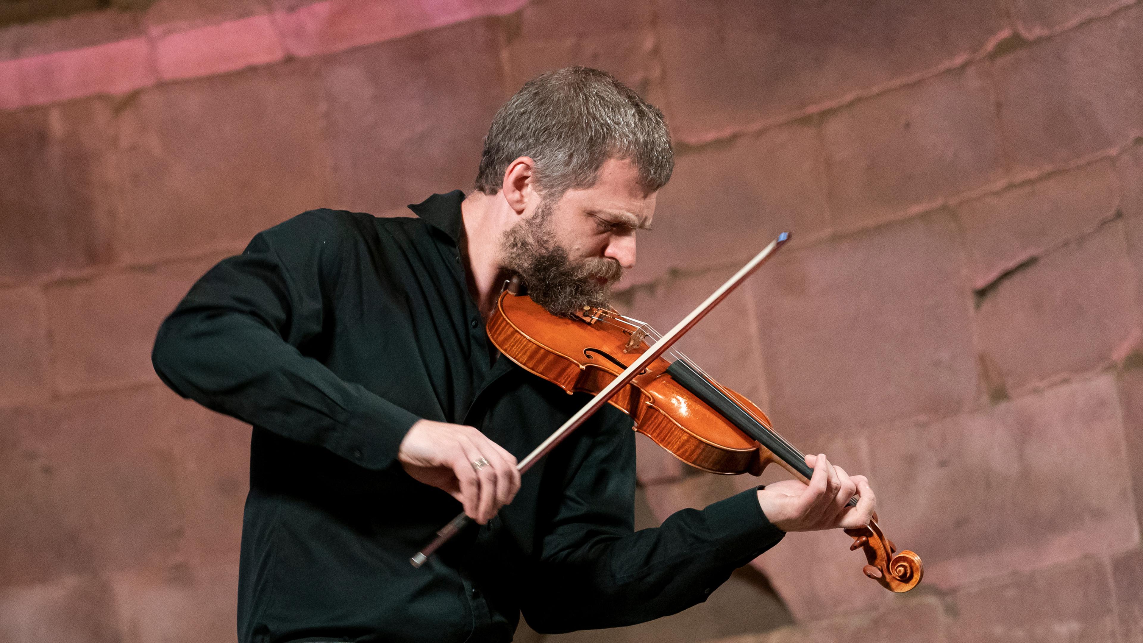 Johnny Gandelsman leans into a violin in performance at The Met Cloisters. He wears a black shirt.