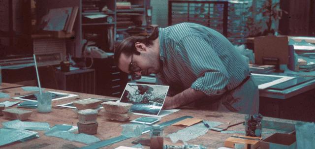 Archival photograph of a conservator working over a work table holding a photograph