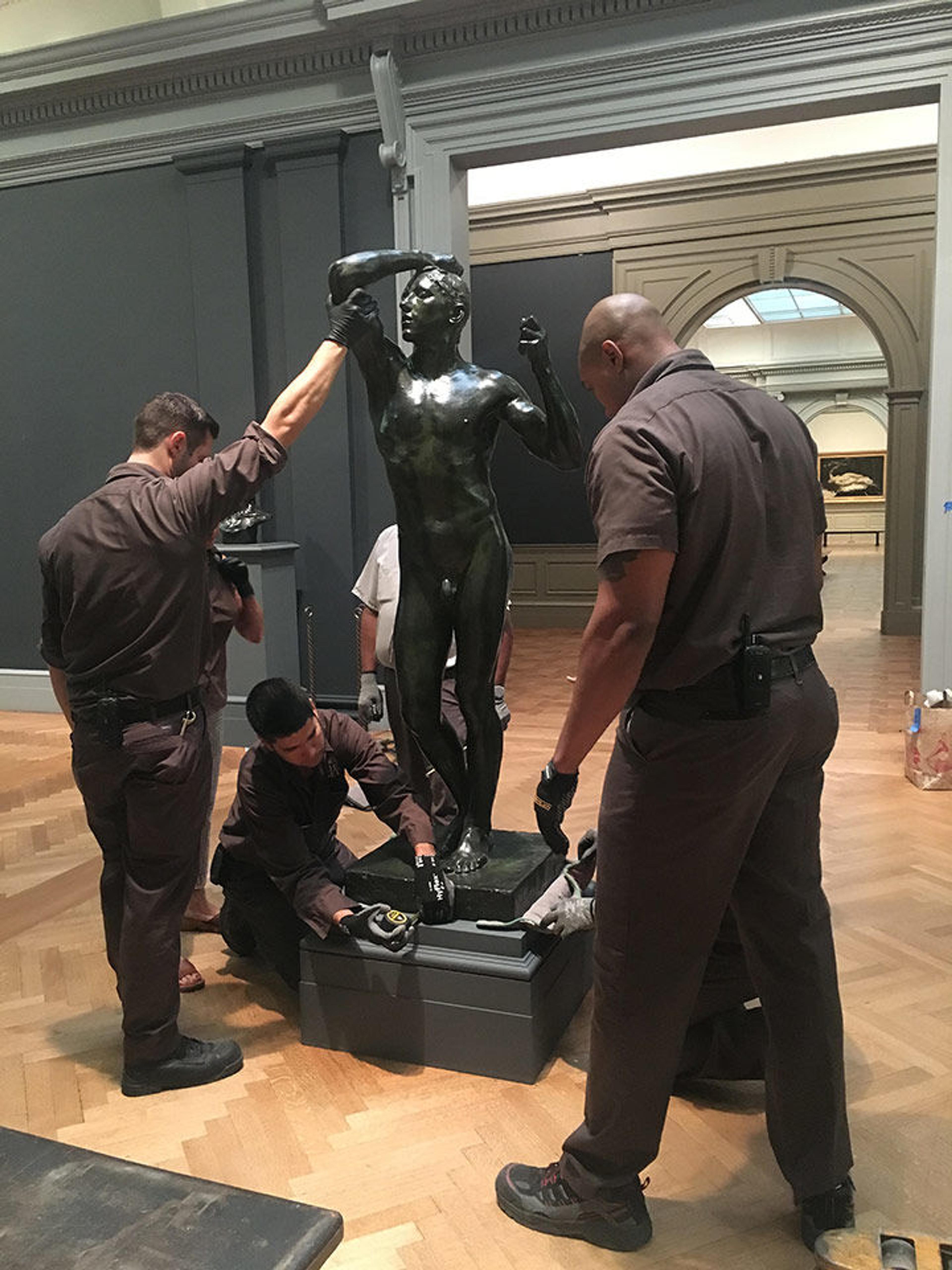 Museum rigger Luis Nuñez takes measurements to center The Age of Bronze on its base. Michael Doscher and Derrick Williams stand to his left and right.
