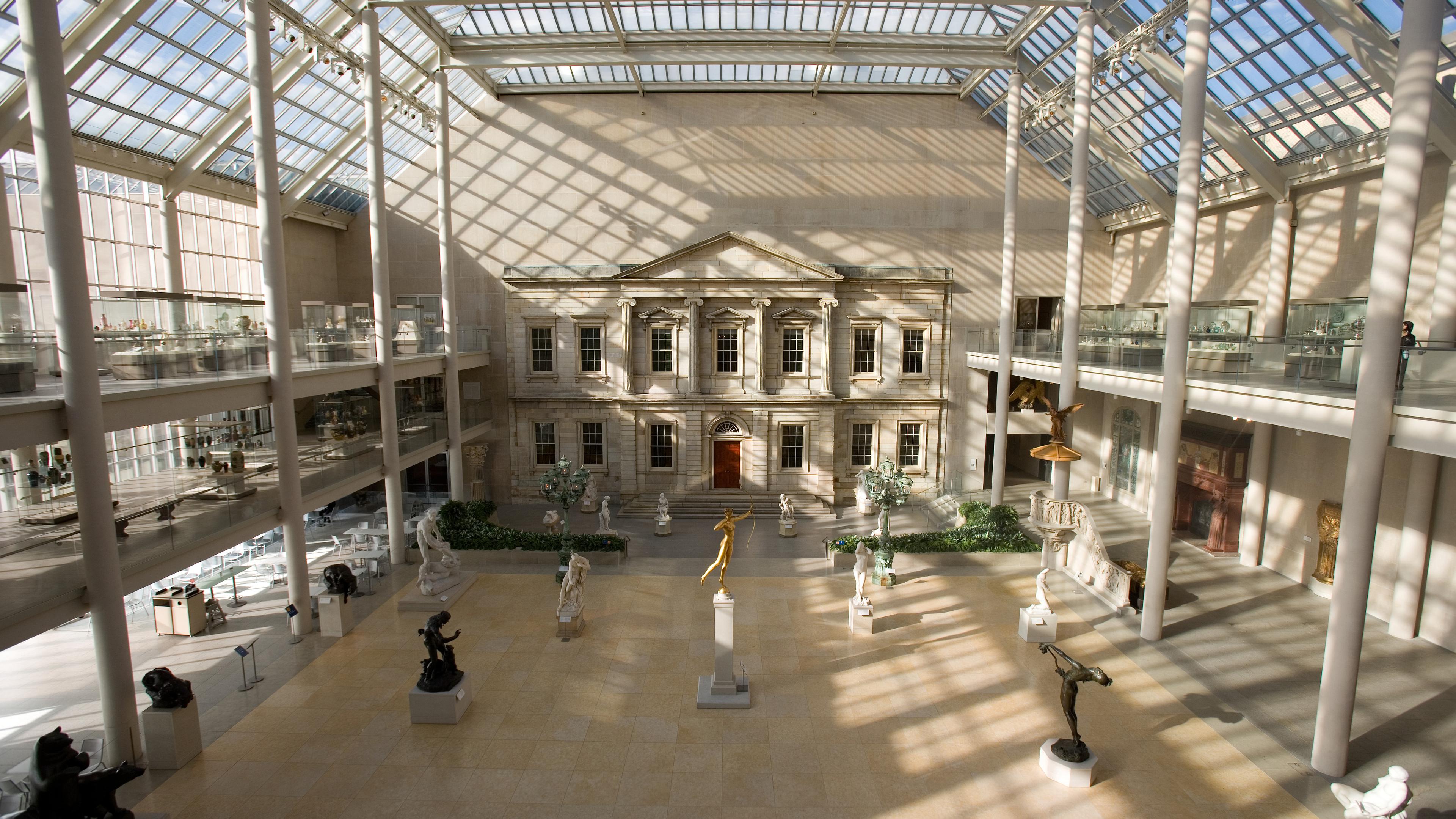 Sculptures displayed throughout a courtyard, neoclassical facade of a building is in the background