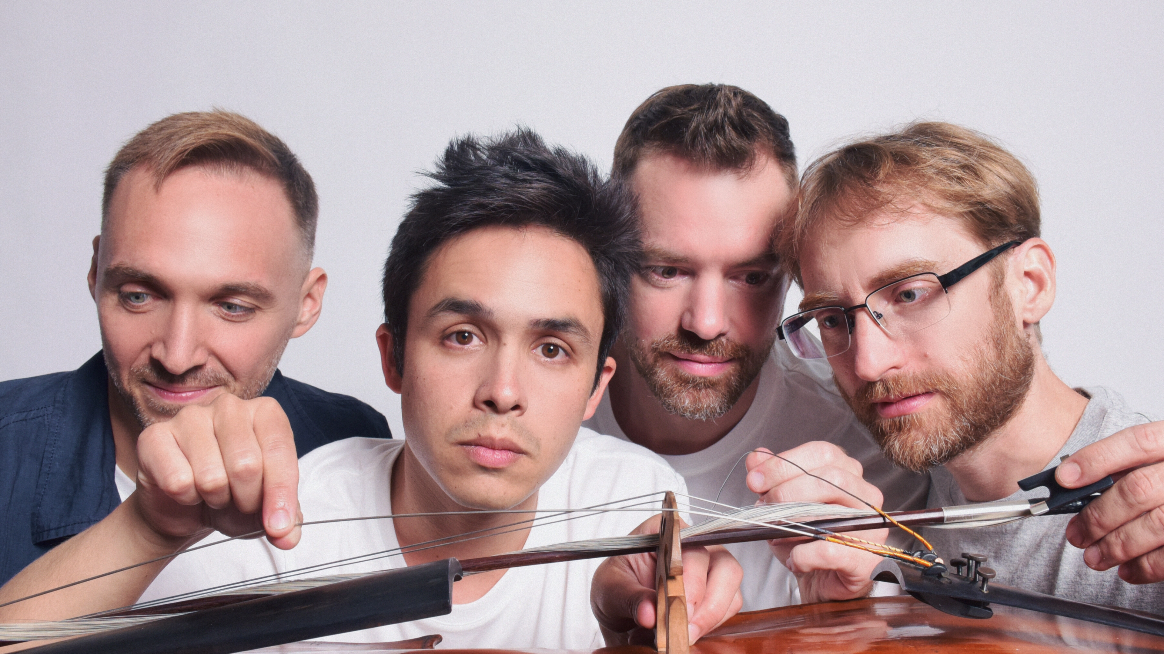 Four men fiddle with the various parts of a cello.