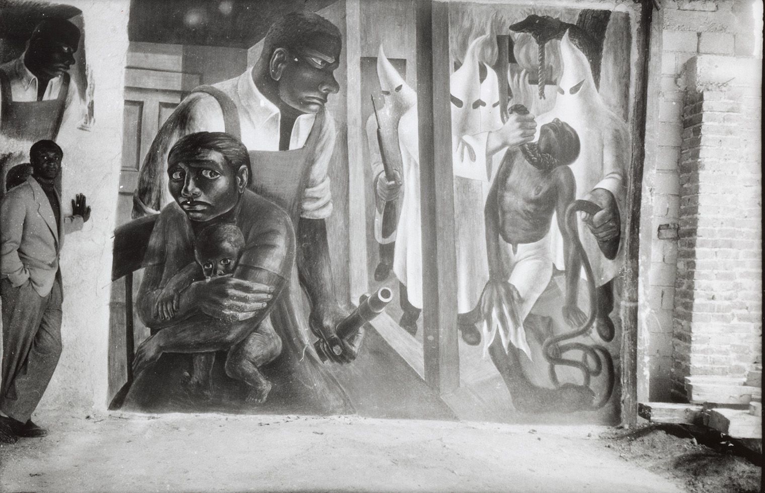 Black and white mural depicting oppression, with a man holding a child, anguished faces, and figures in hoods and robes.