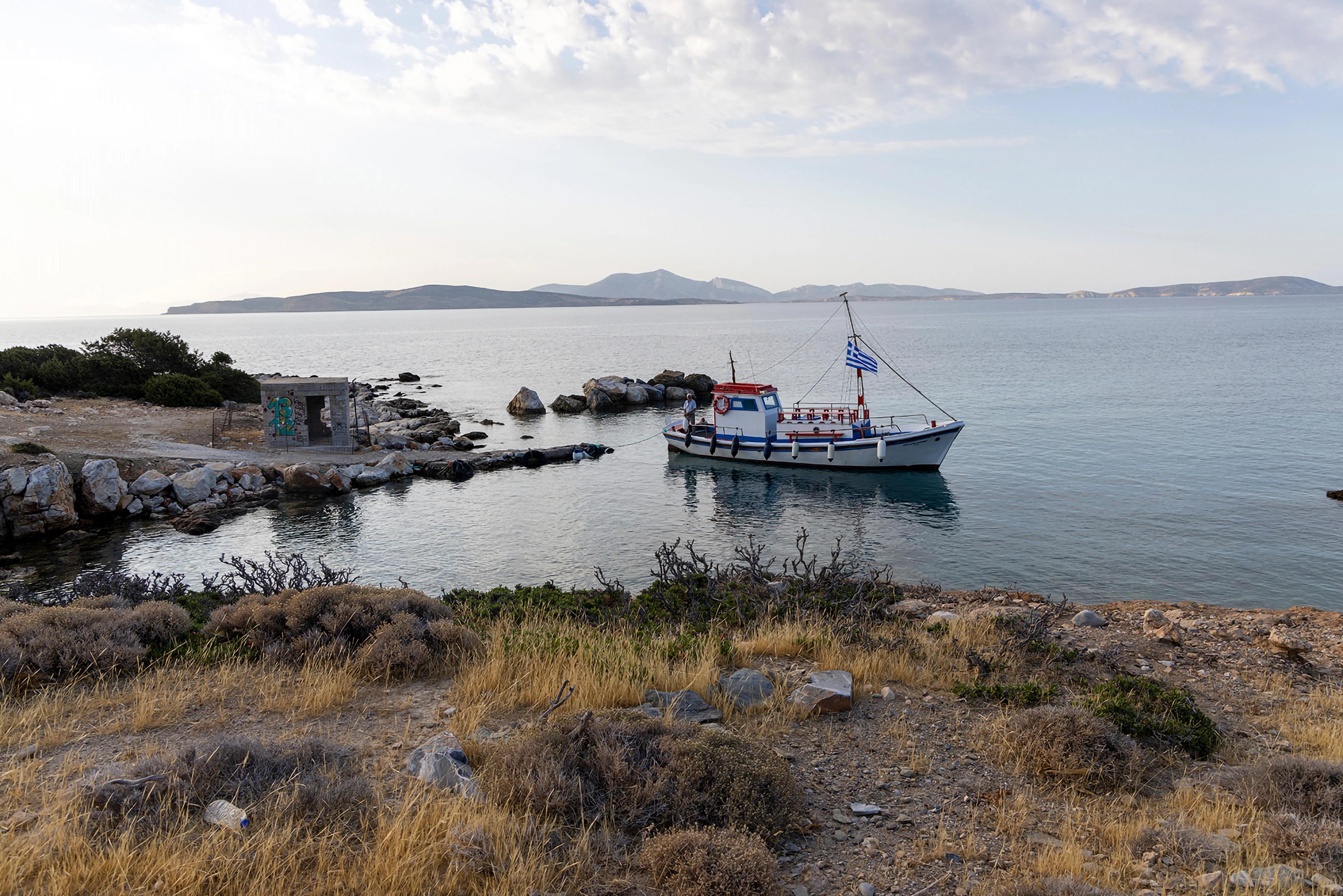 Sailboat anchored along a rocky, brushy shoreline.
