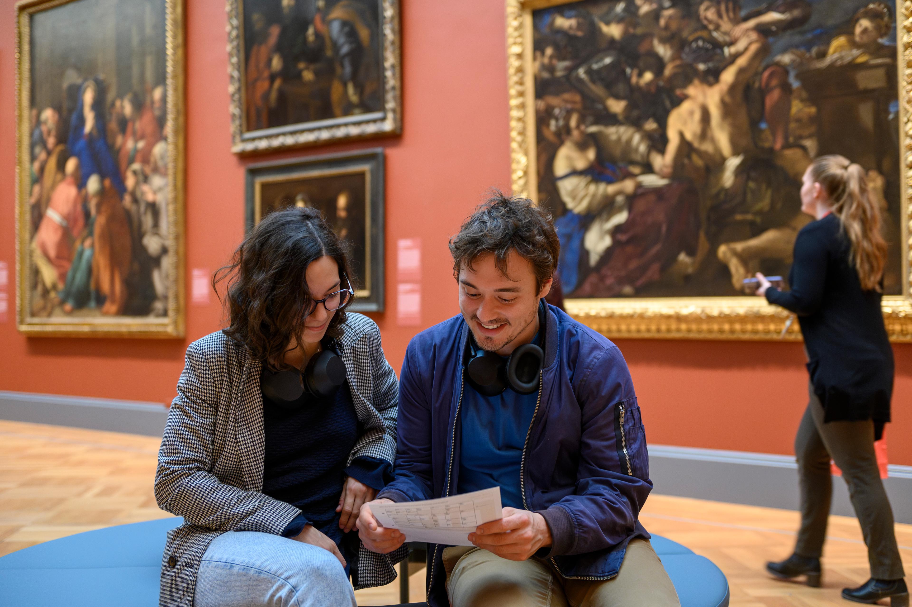 A man and woman sit together and look at a museum map in The Met's European Paintings galleries. 