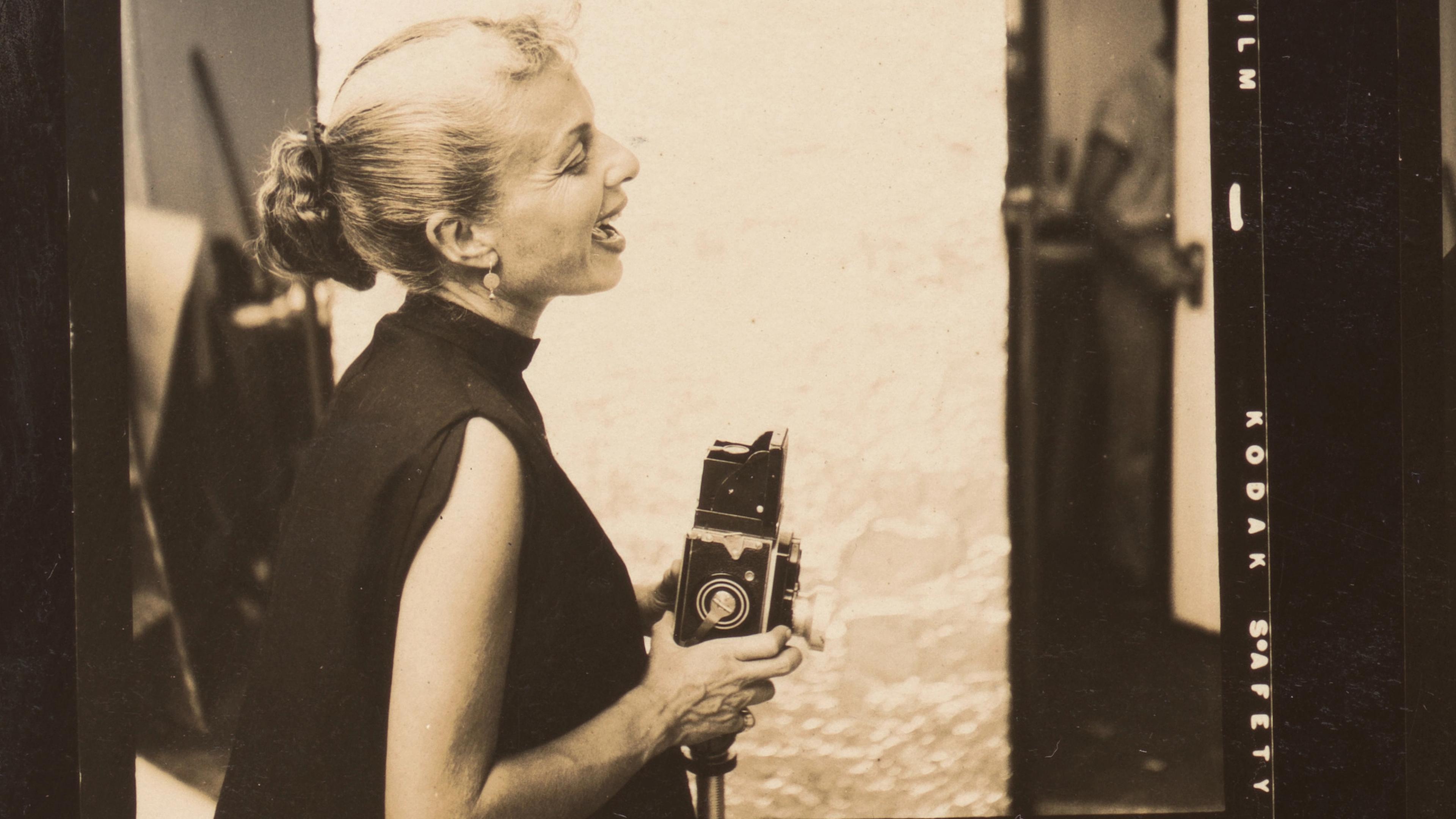 A glamorous-looking woman caught mid-laugh. She holds a camera.
