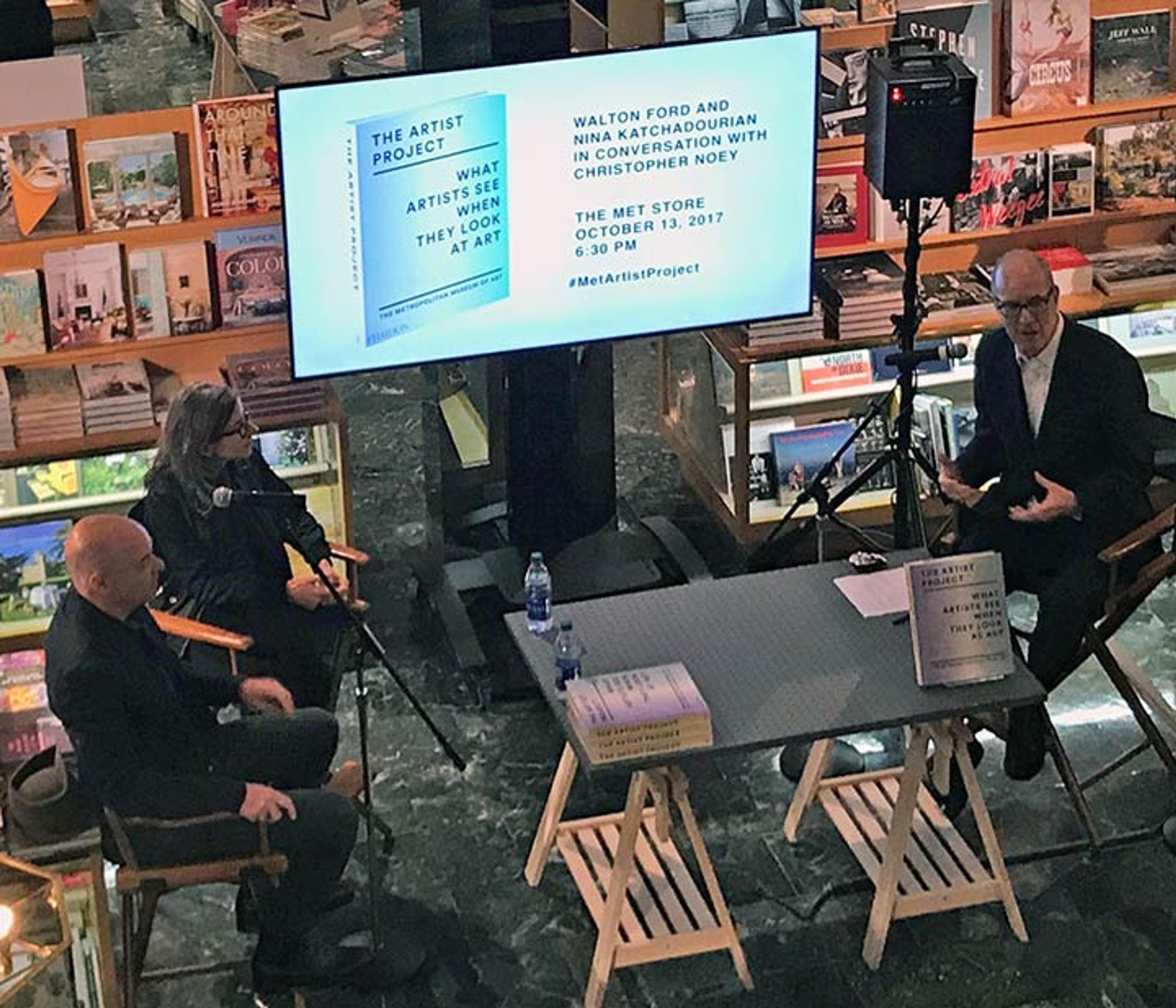 Three people having a conversation at a table in the Met Store in front of a projection screen