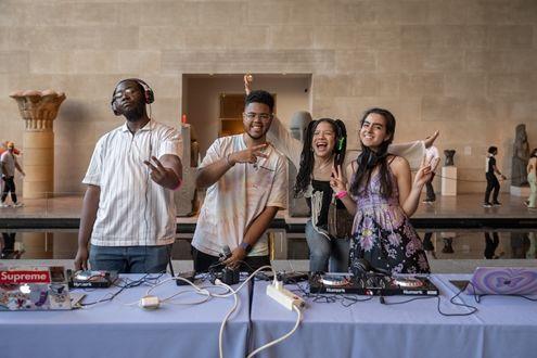 Four young adults pose in front of a table with DJ equipment