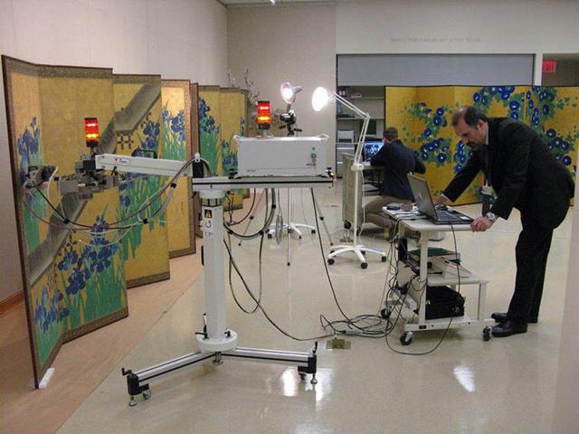 A conservator carrying out instrumental analysis of an object with a mobile X-ray fluorescence spectrometer.