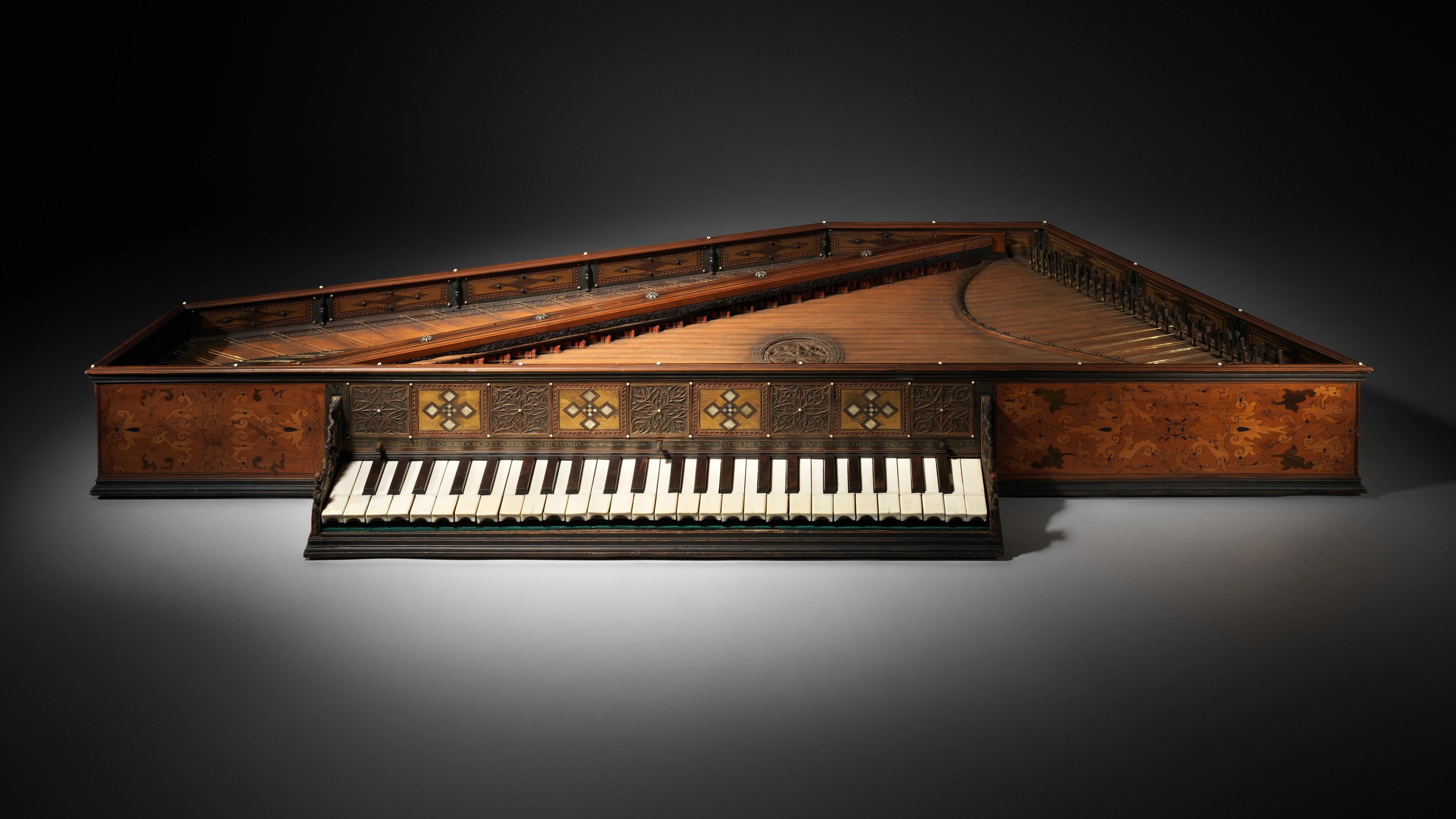 Triangular wooden harpsichord with ornate inlay and a single keyboard, shown against a dark background.