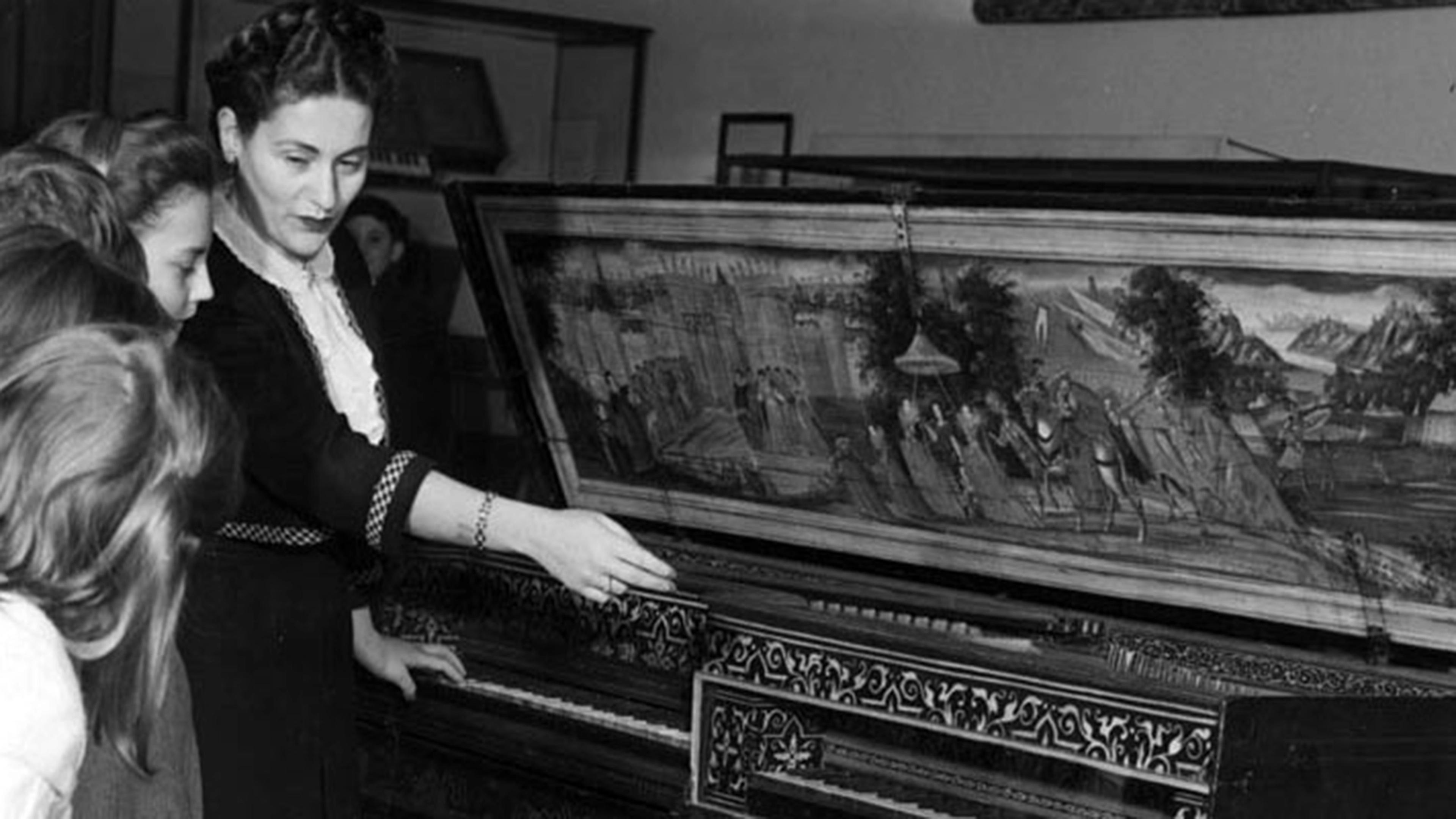 A woman showing an instrument with an ornately painted lid to a group of children.