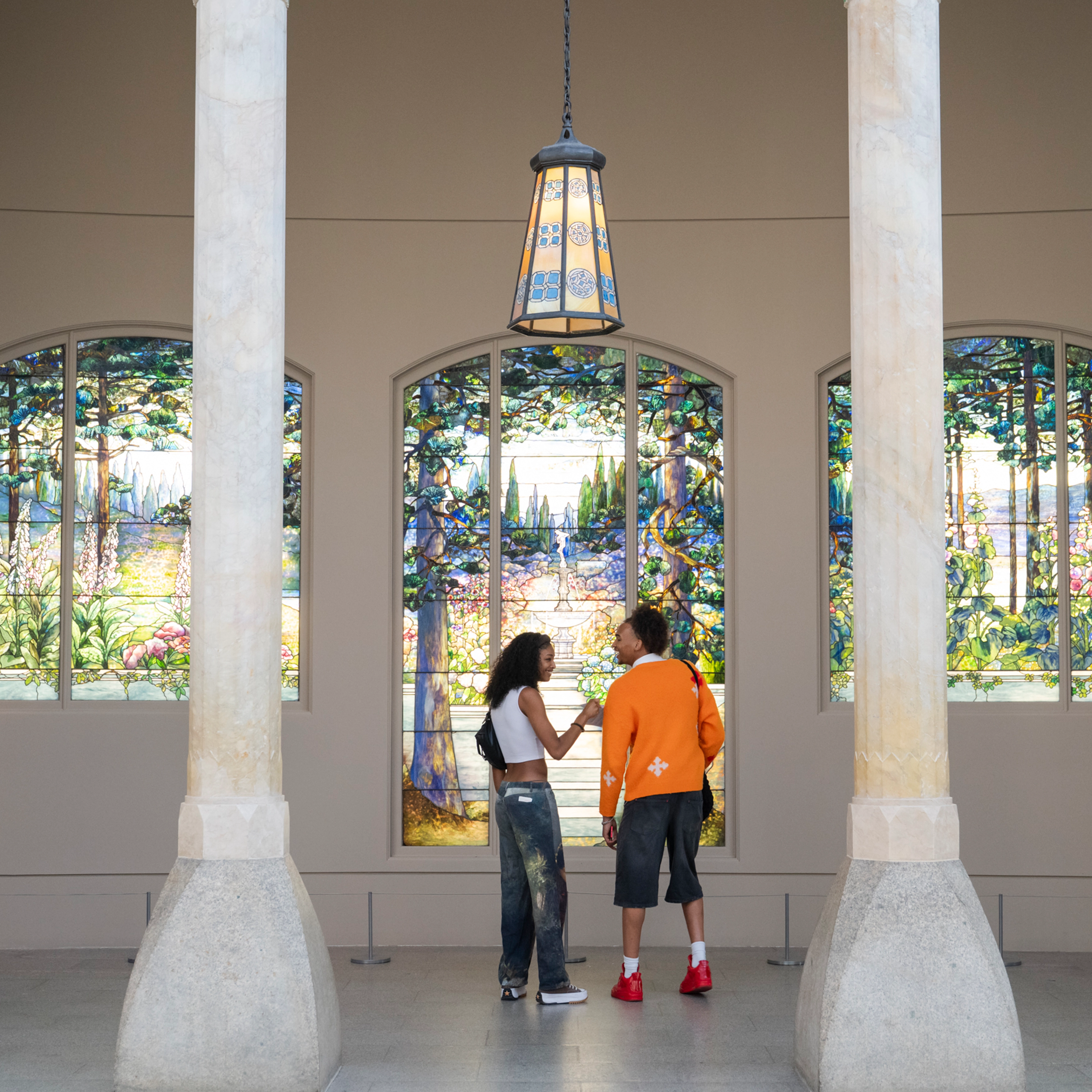 Two people in front of the 3-part Garden landscape window for Linden Hall. Gallery 701, The Metropolitan Museum of Art.  
