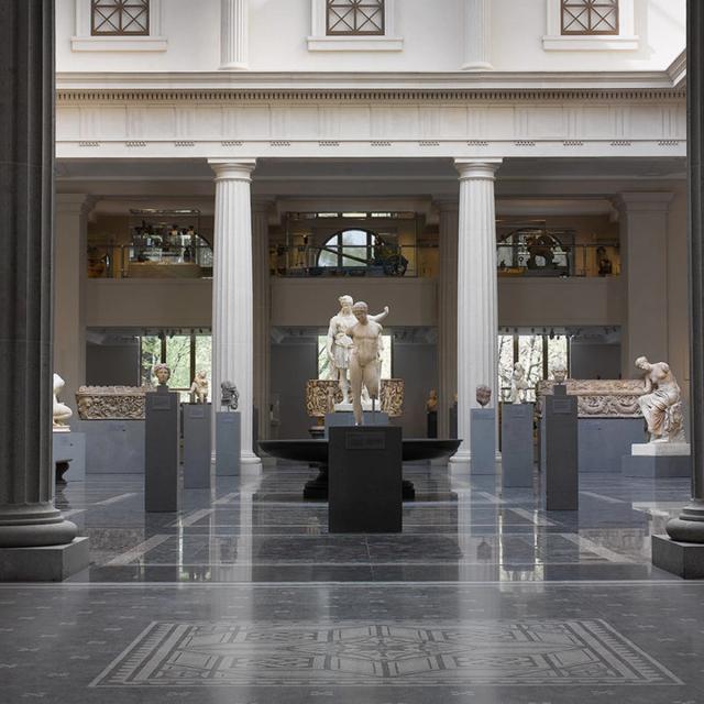 A view of the Greek and Roman Galleries in soft daylight with no visitors. The contrasts of the black floor and pedestals and white stone statues and columns creates a dramatic image.