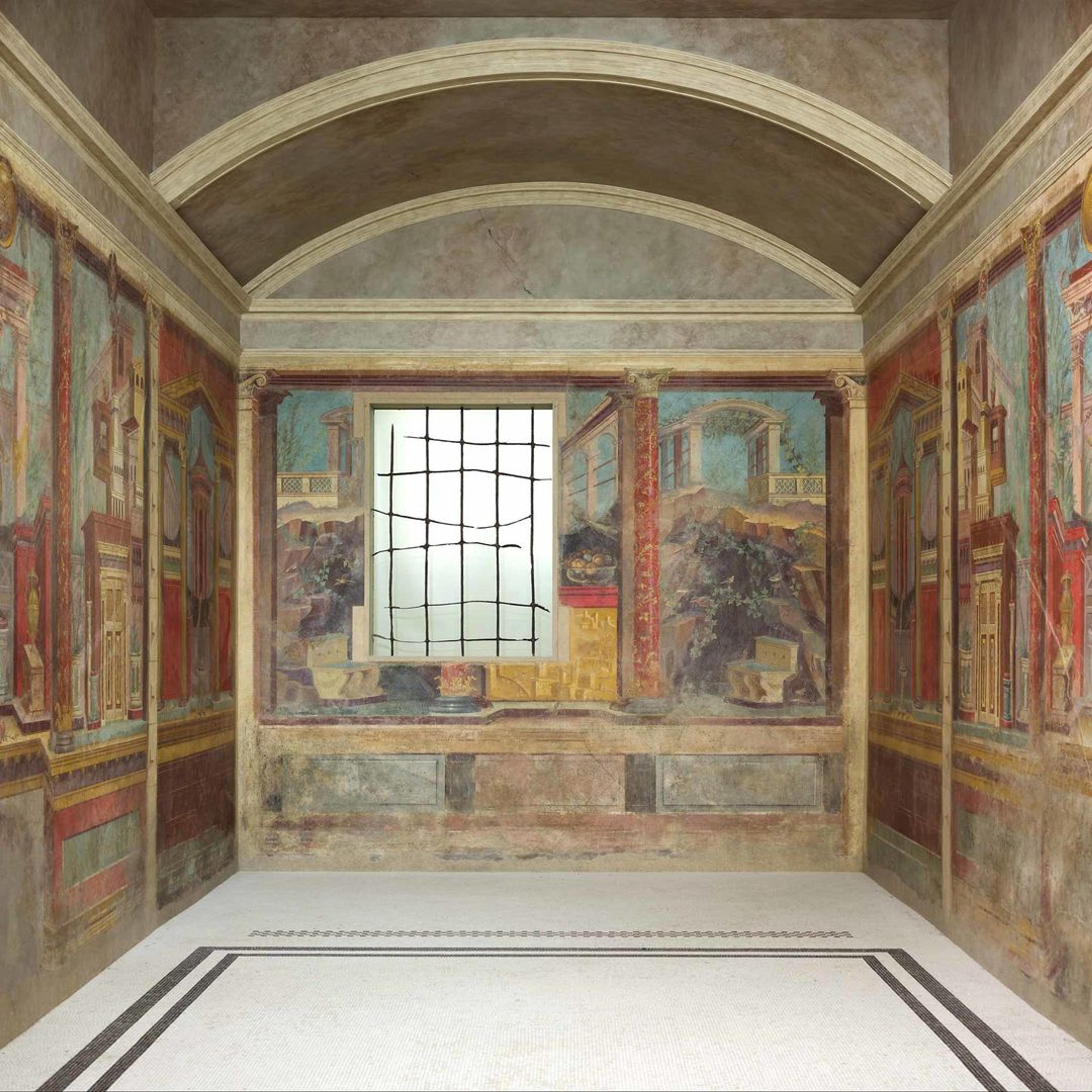 An ornate Roman-style room with painted frescoes depicting architectural and natural scenes, framed by columns and arches, with a central window featuring a grid design letting in soft light