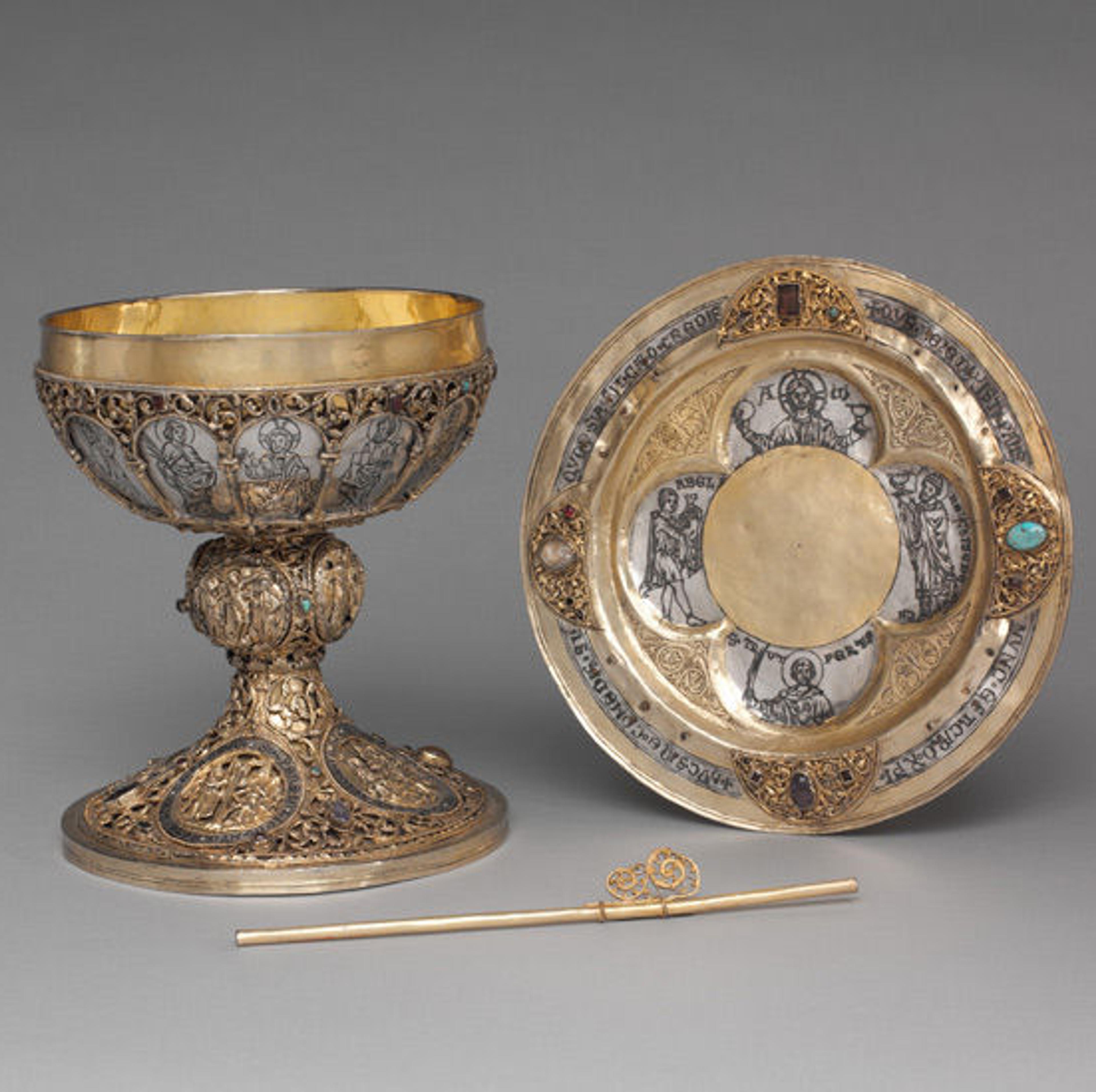Chalice, plate, and straw ornately made of gold with religious imagery.