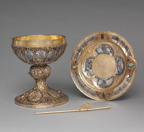Chalice, plate, and straw ornately made of gold with religious imagery.