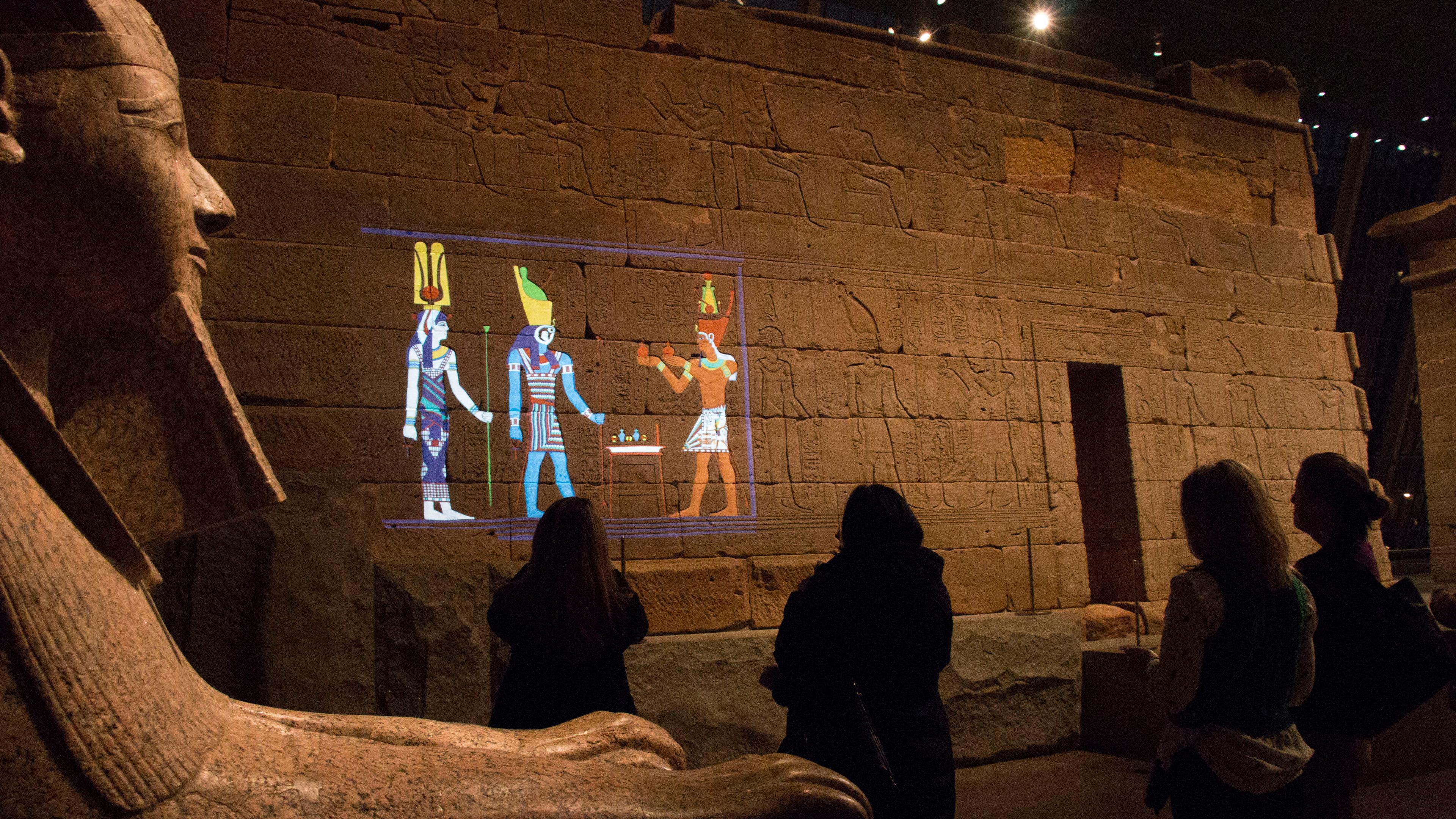 Visitors viewing a colorful projection on the wall of the Temple of Dendur at The Metropolitan Museum of Art