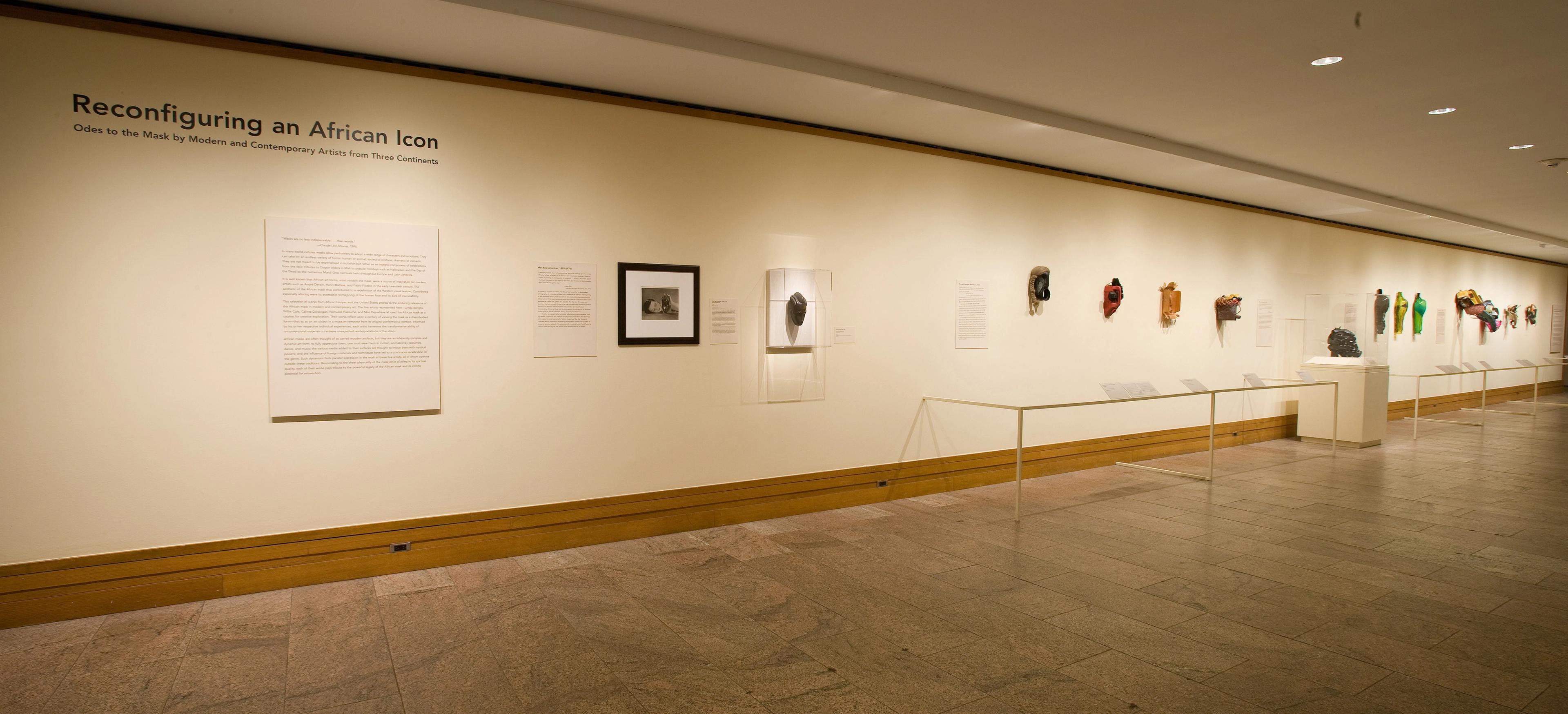 A row of African masks hanging on a white gallery wall.