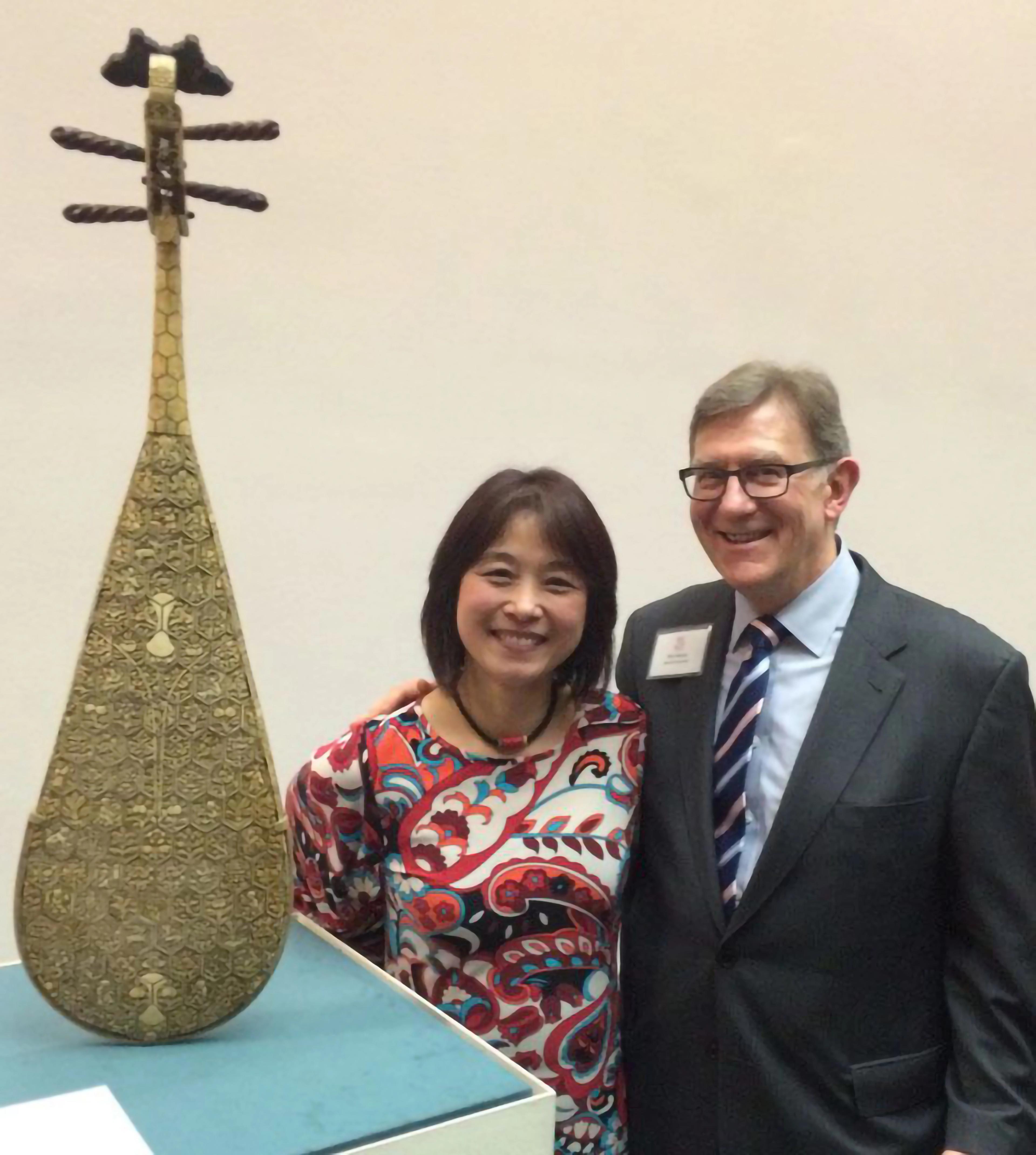 Wu Man and Ken Moore stand smiling next to an ornate pipa elevated on a pedestal.