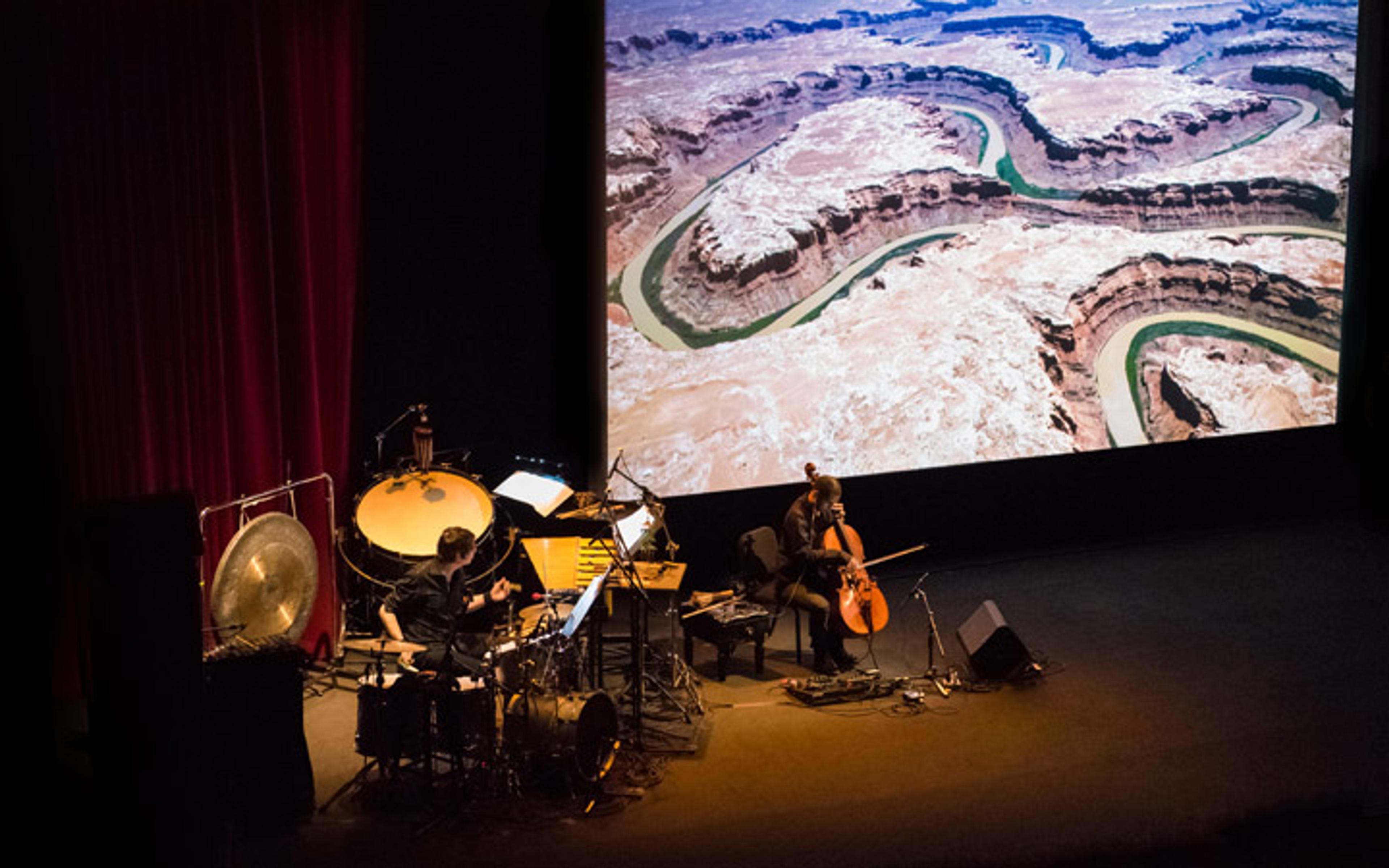 On a darkened stage several musicians perform before a screen projection of a film depicting the Colorado River basin