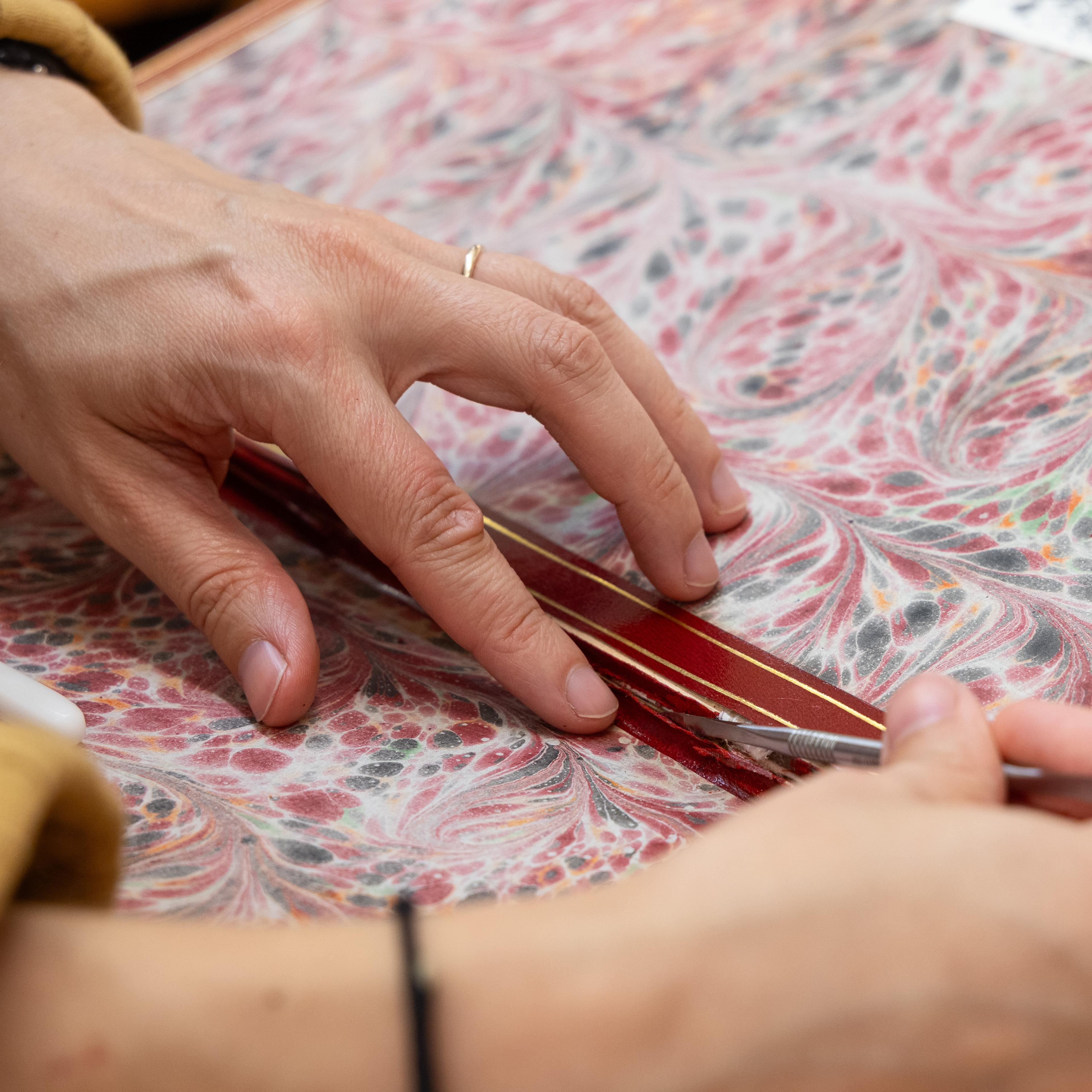 A close up of the hands of a book conservator who is reattaching the leather hinge of a book.