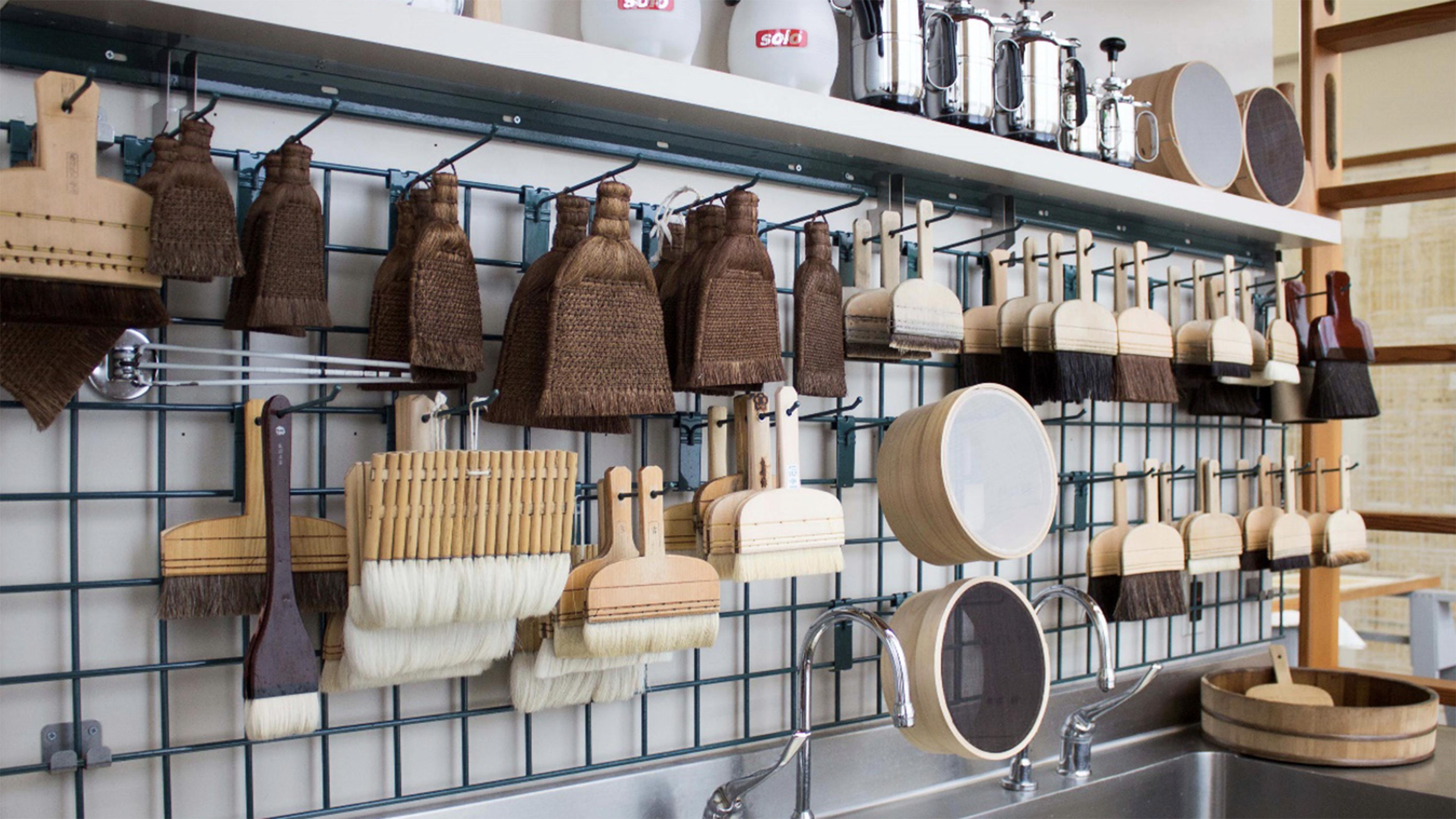 A collection of a variety of conservation brushes and tools suspended on a wall-mounted rack.