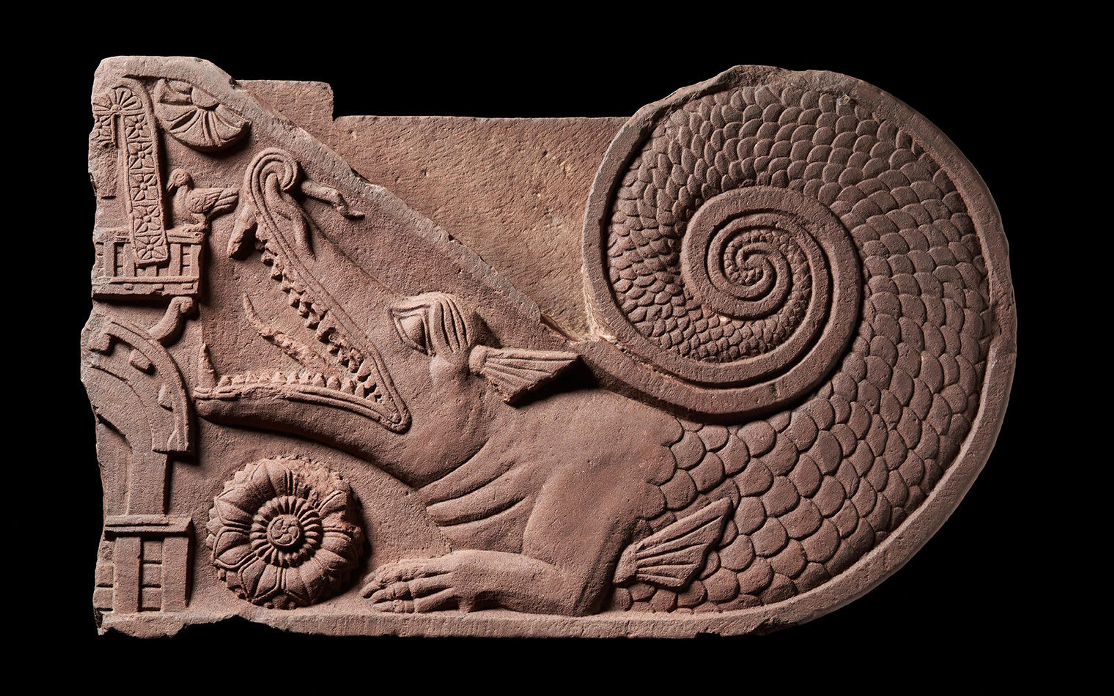 Sandstone carving of a beast with its mouth open and a scaled tail