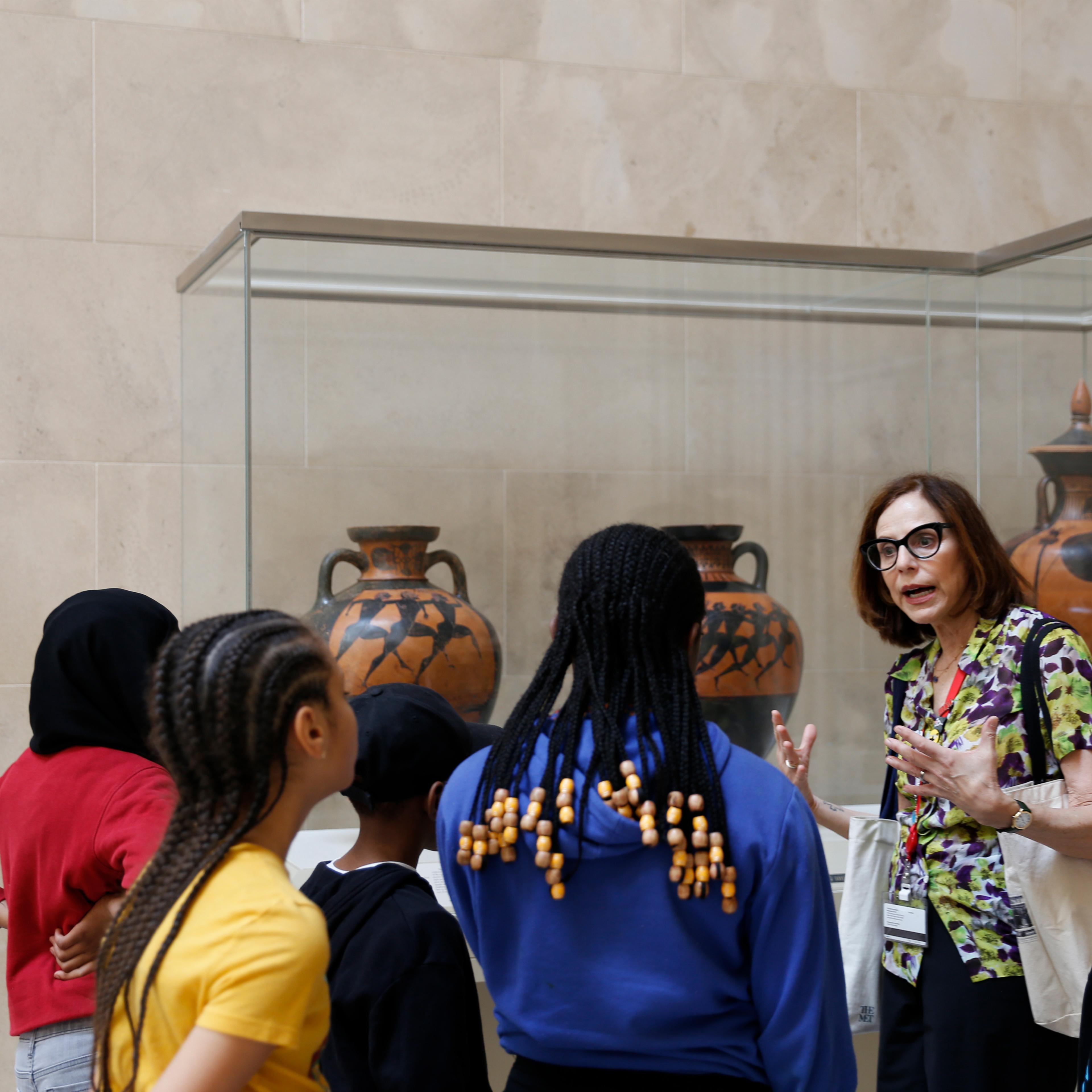 A group of young kids being led through the Greek and Roman Galleries by a docent.