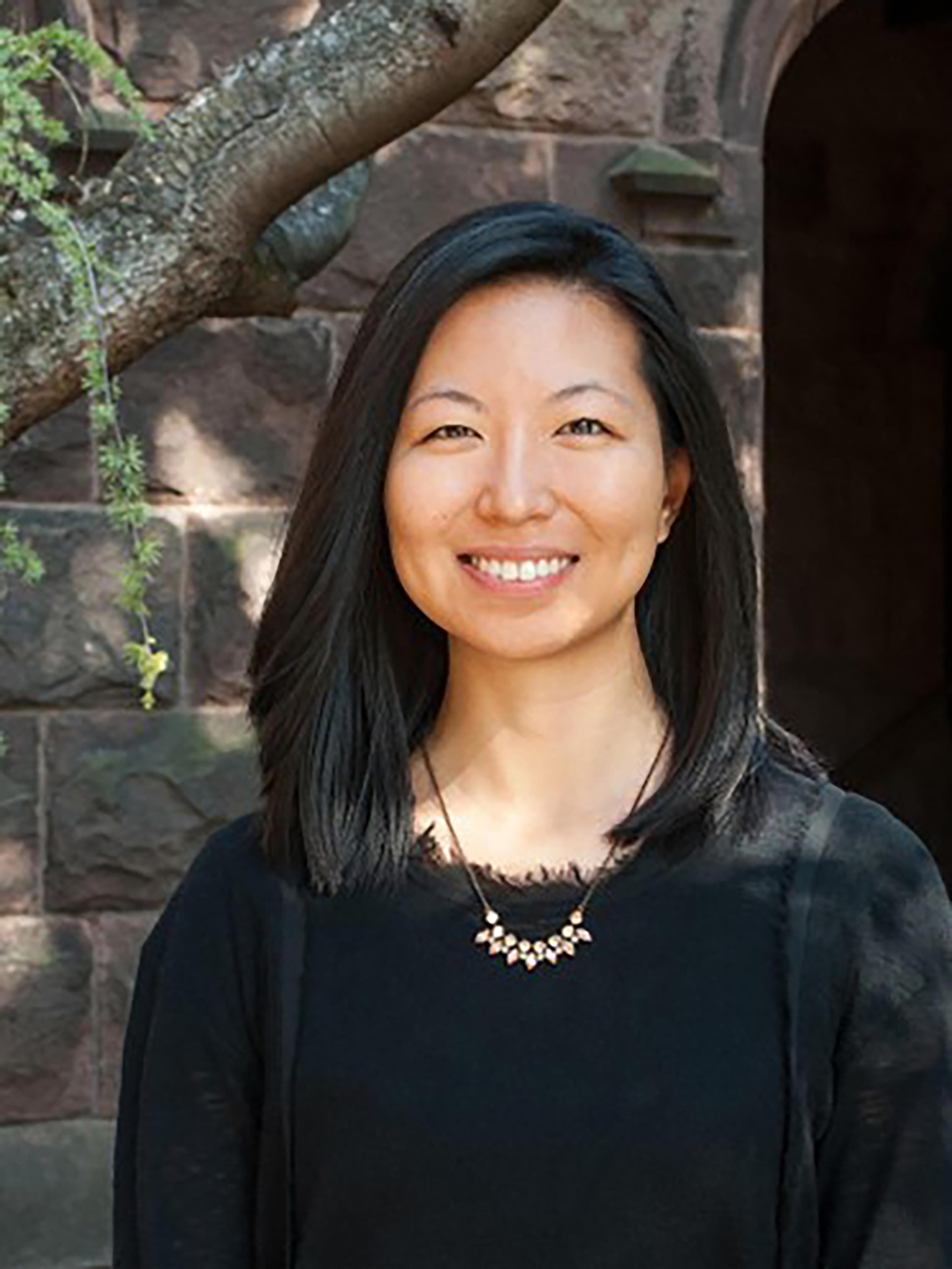 A woman with shoulder length black hair smiles in front of a stone building