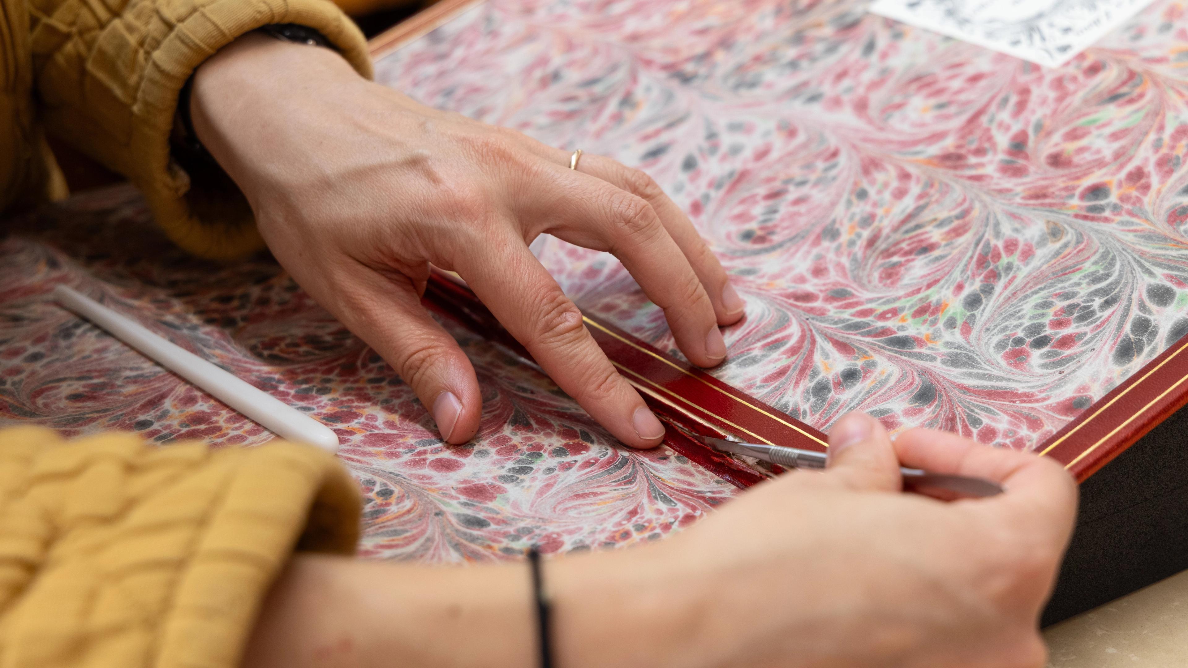 A close up of the hands of a book conservator who is reattaching the leather hinge of a book.