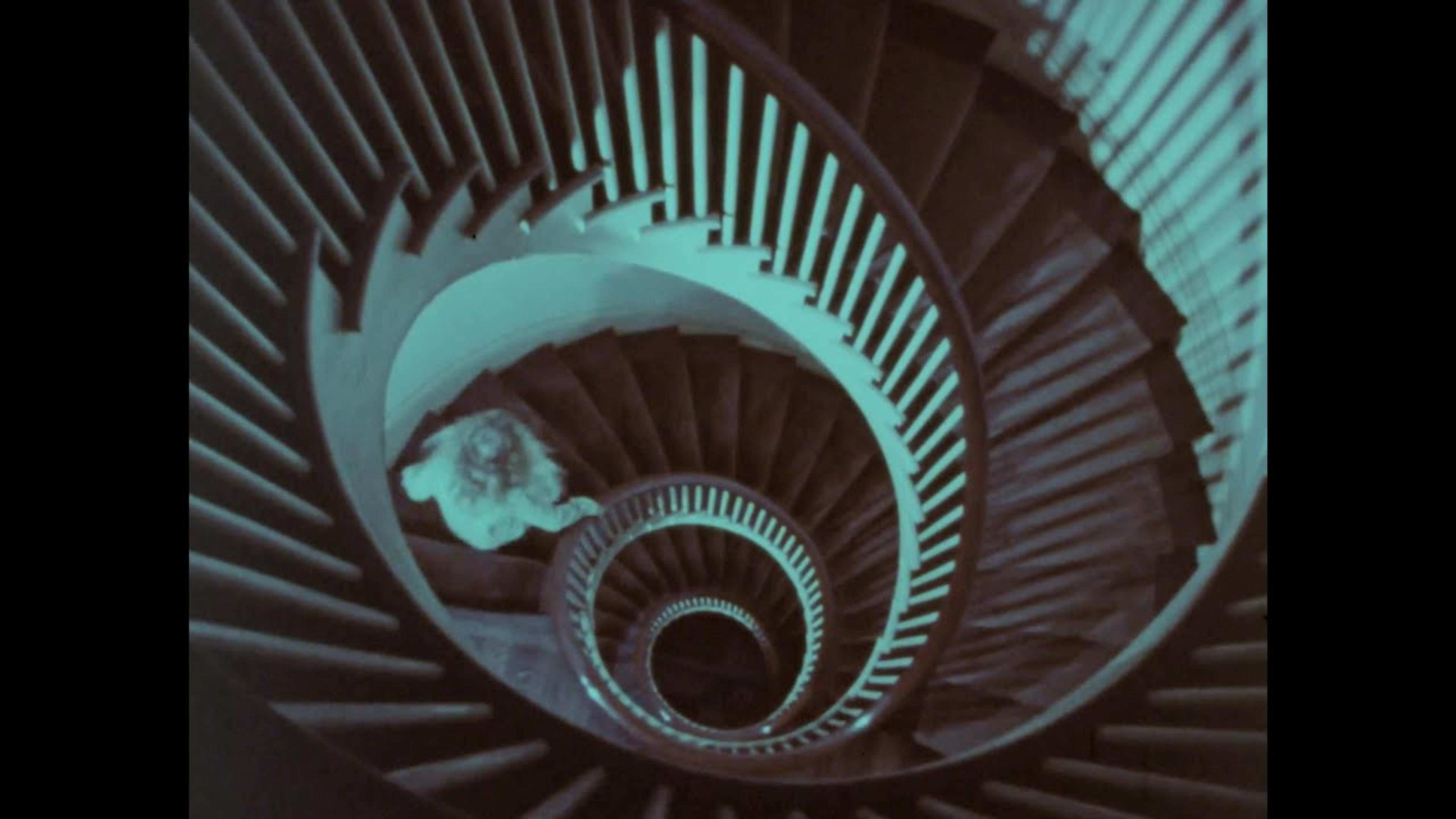 A top-down view of a spiral staircase with a person descending, creating a mesmerizing, infinite loop effect.