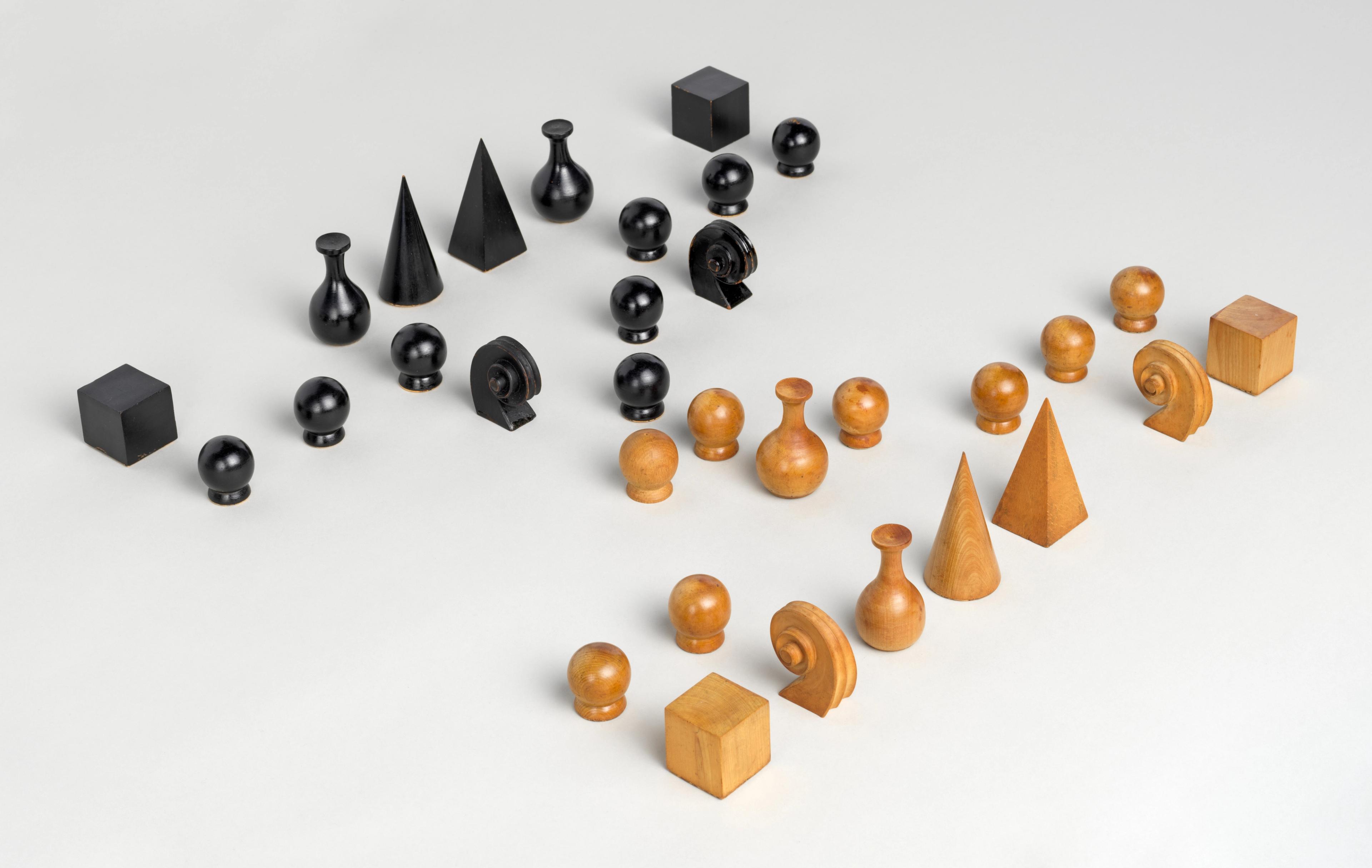 Black and natural wood chess pieces with geometric shapes arranged in two opposing groups on a white surface.