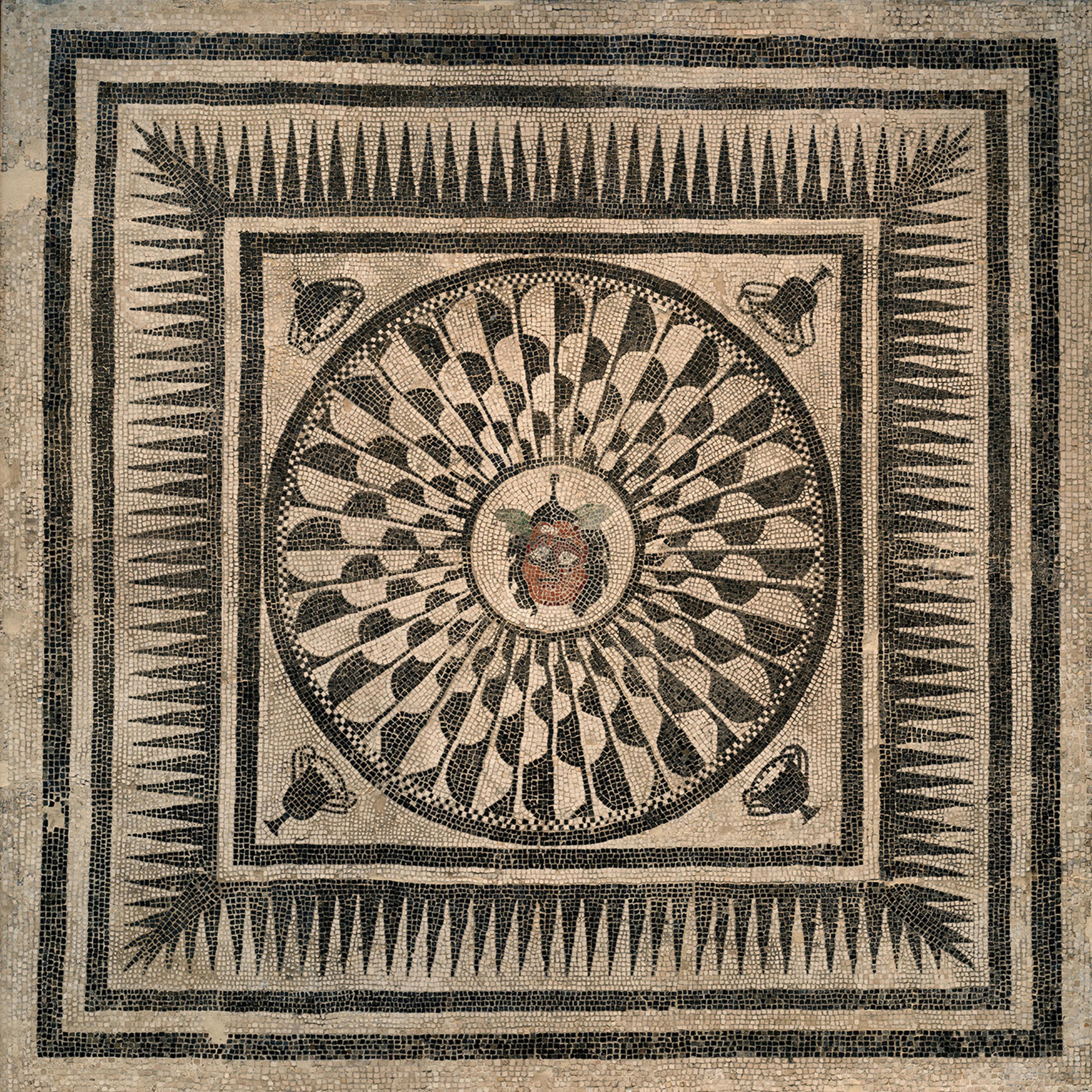 Ancient mosaic featuring a central Medusa head, radiating petal-like patterns, geometric borders, and four corner masks on a stone background.