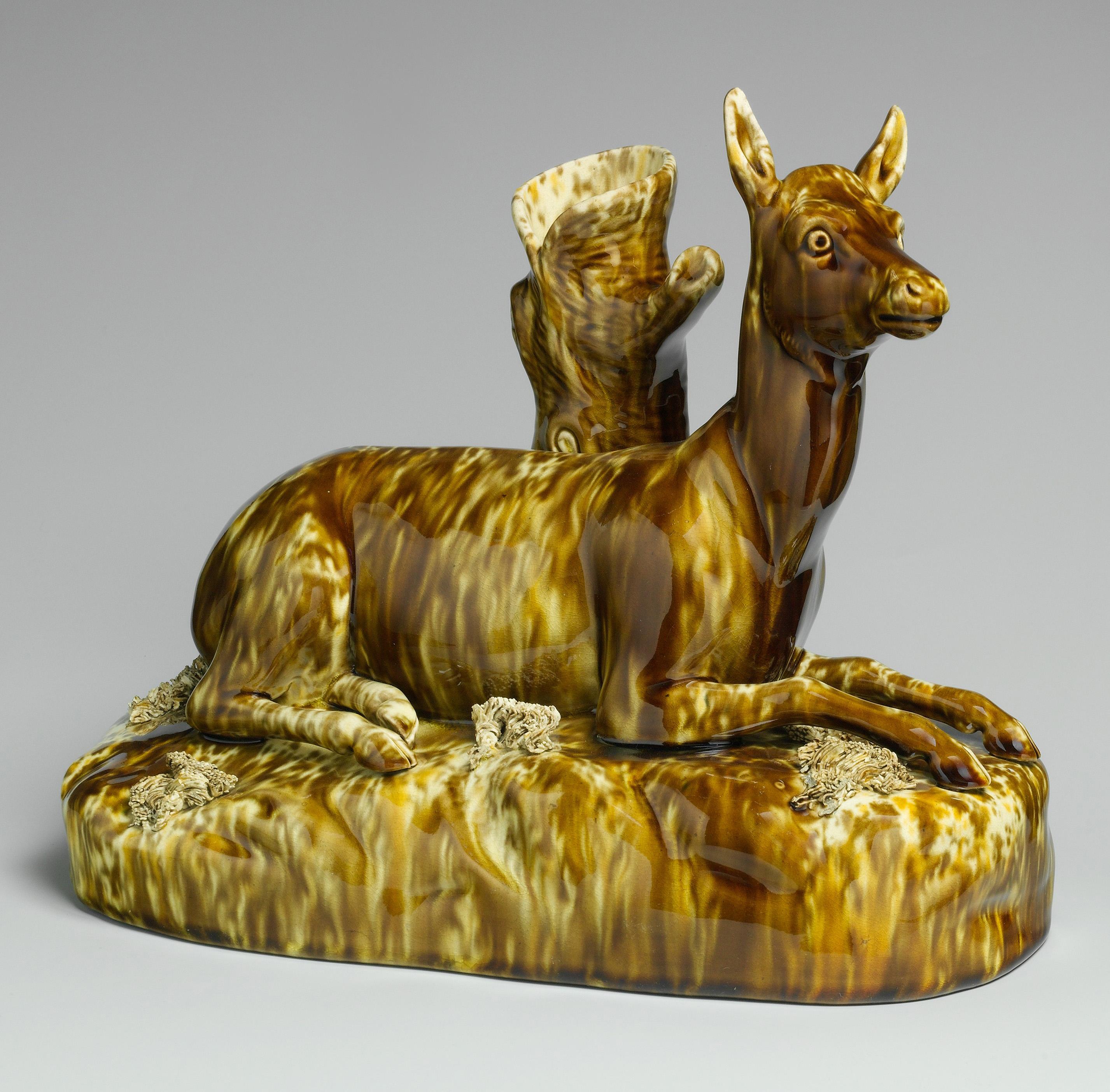 Figurine of a reclining deer covered with an allover mottled brown enameled glaze.