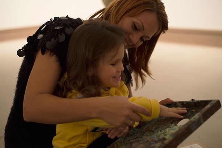 Smiling woman guides the hands of a young girl across an art object.
