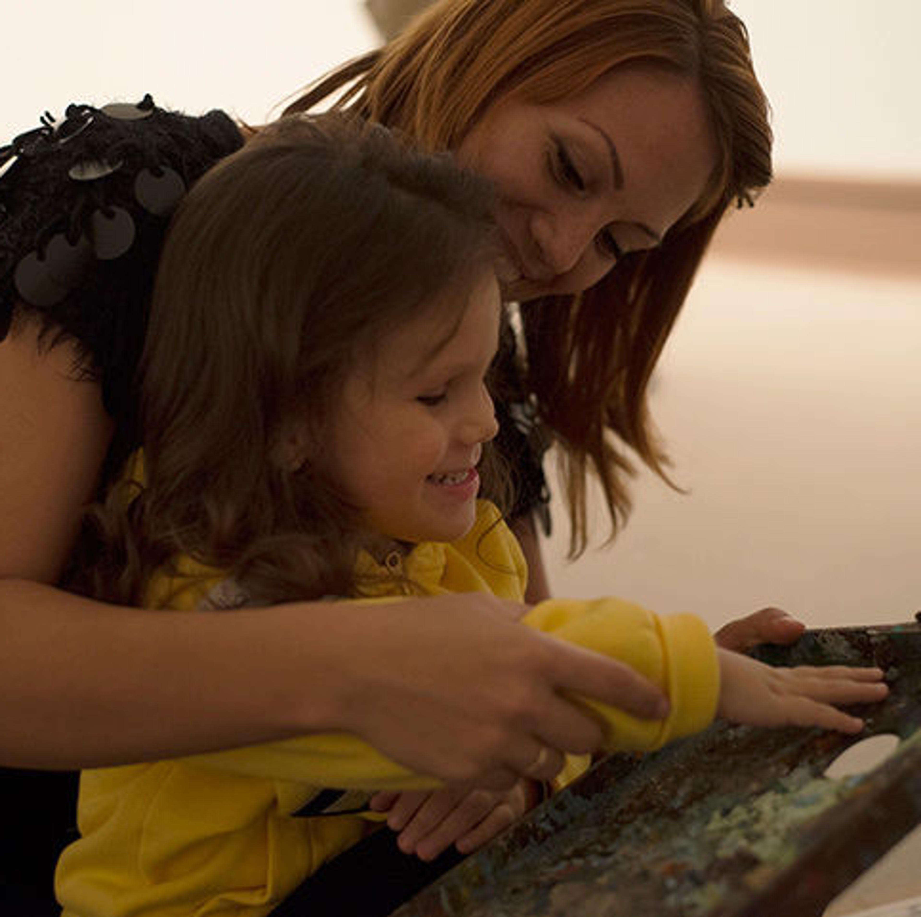 Smiling woman guides the hands of a young girl across an art object.