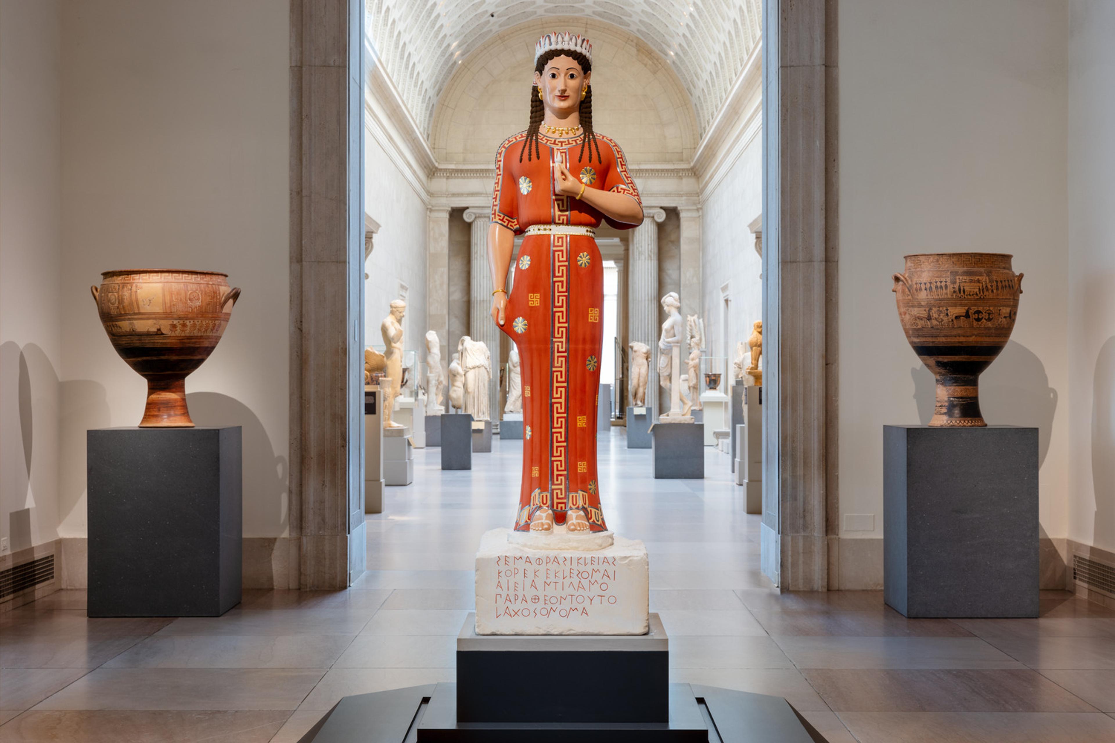 A polychrome statue of a woman in a read dress stands in stark contrast to the muted colors in The Met's Greek and Roman Galleries.