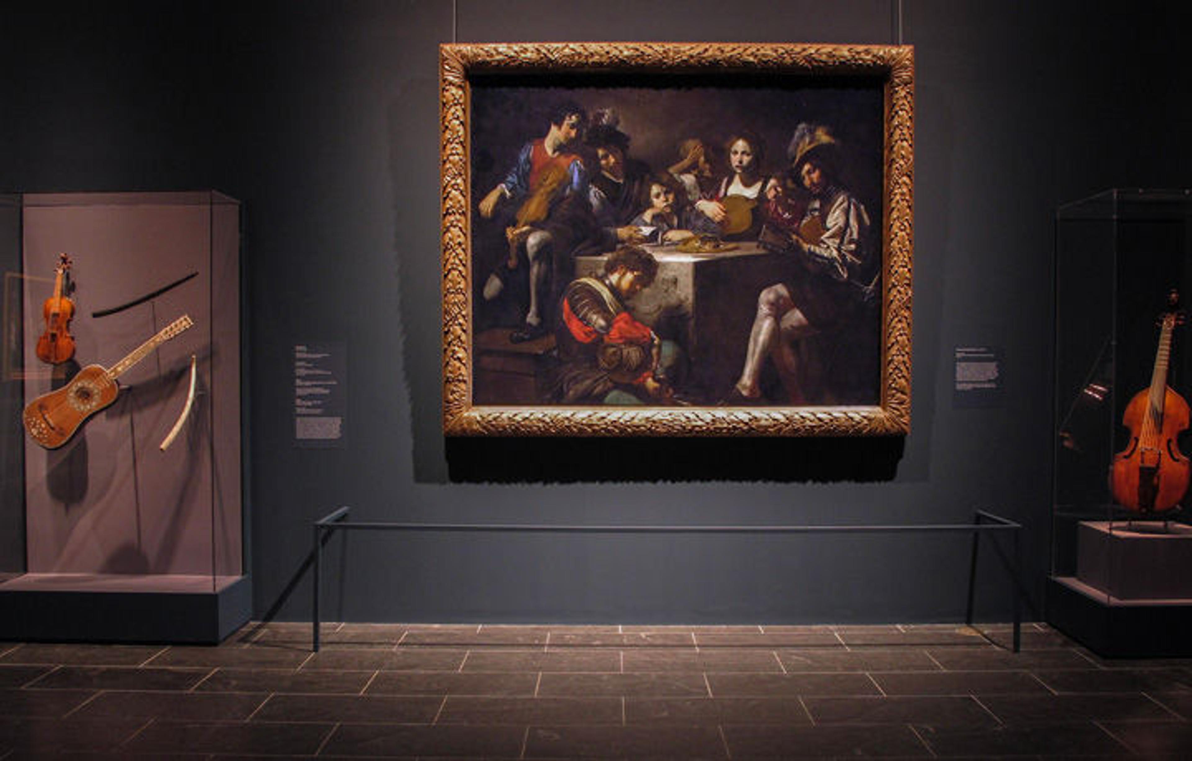 Gallery view of the exhibition "Valentin de Boulogne: Beyond Caravaggio" showing an oil painting flanked by three musical instruments from the artist's period
