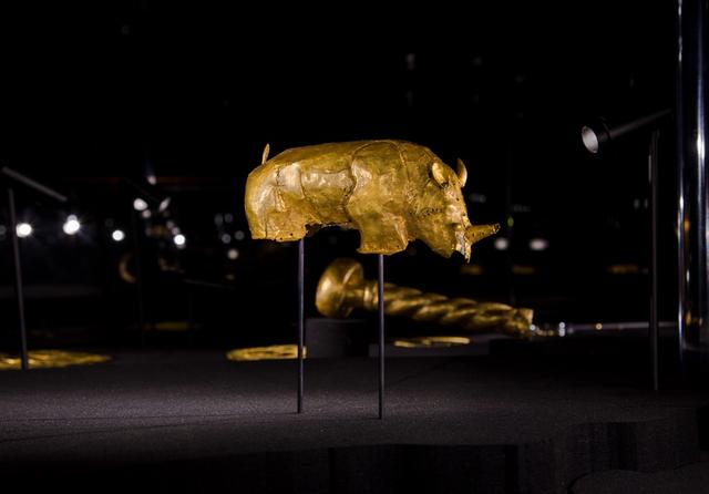 A golden rhinoceros against a dark backdrop, installed alongside a small cache of other royal emblems, including a golden scepter