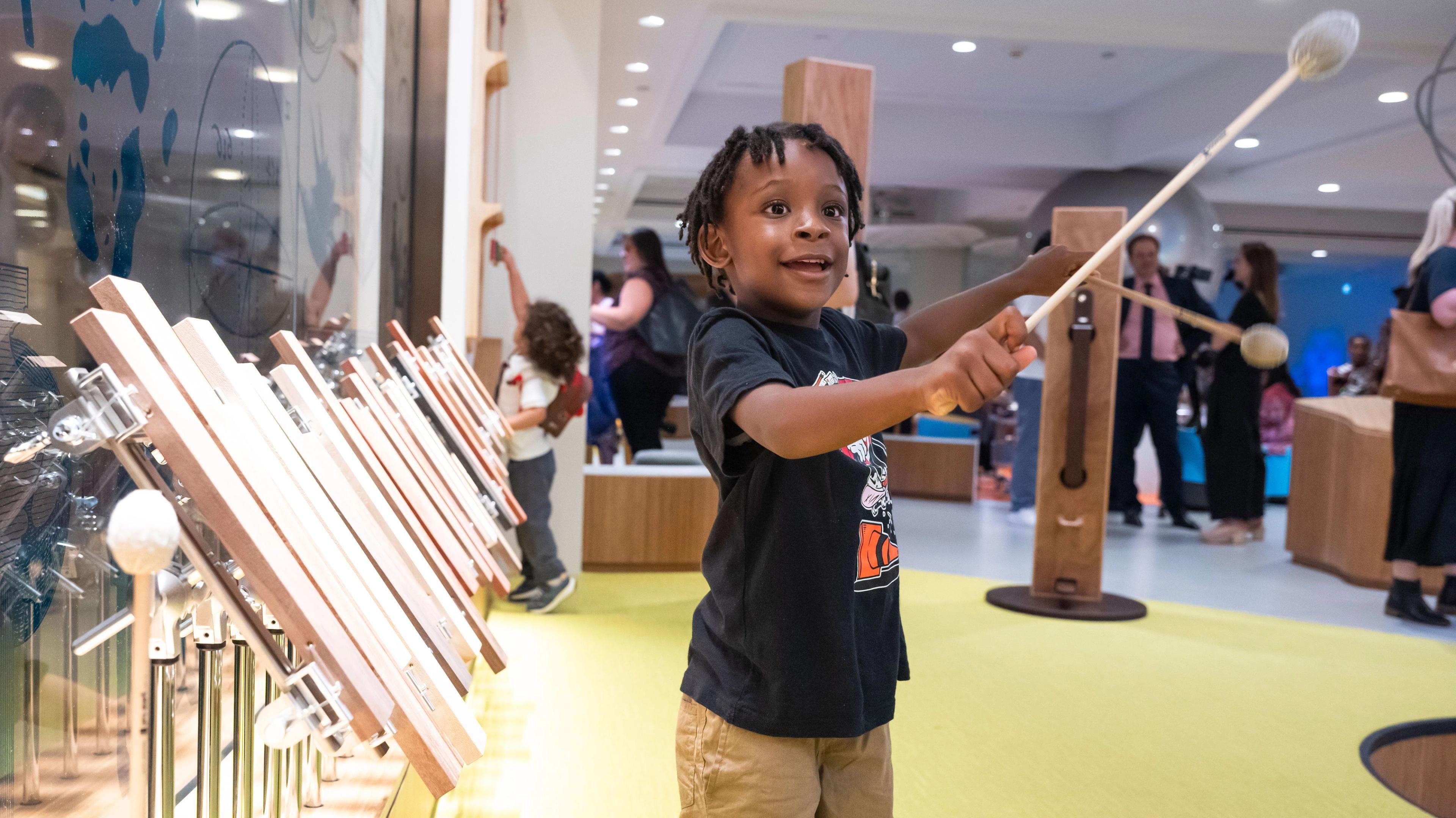 A young child stands in front of a xylophone with mallets.