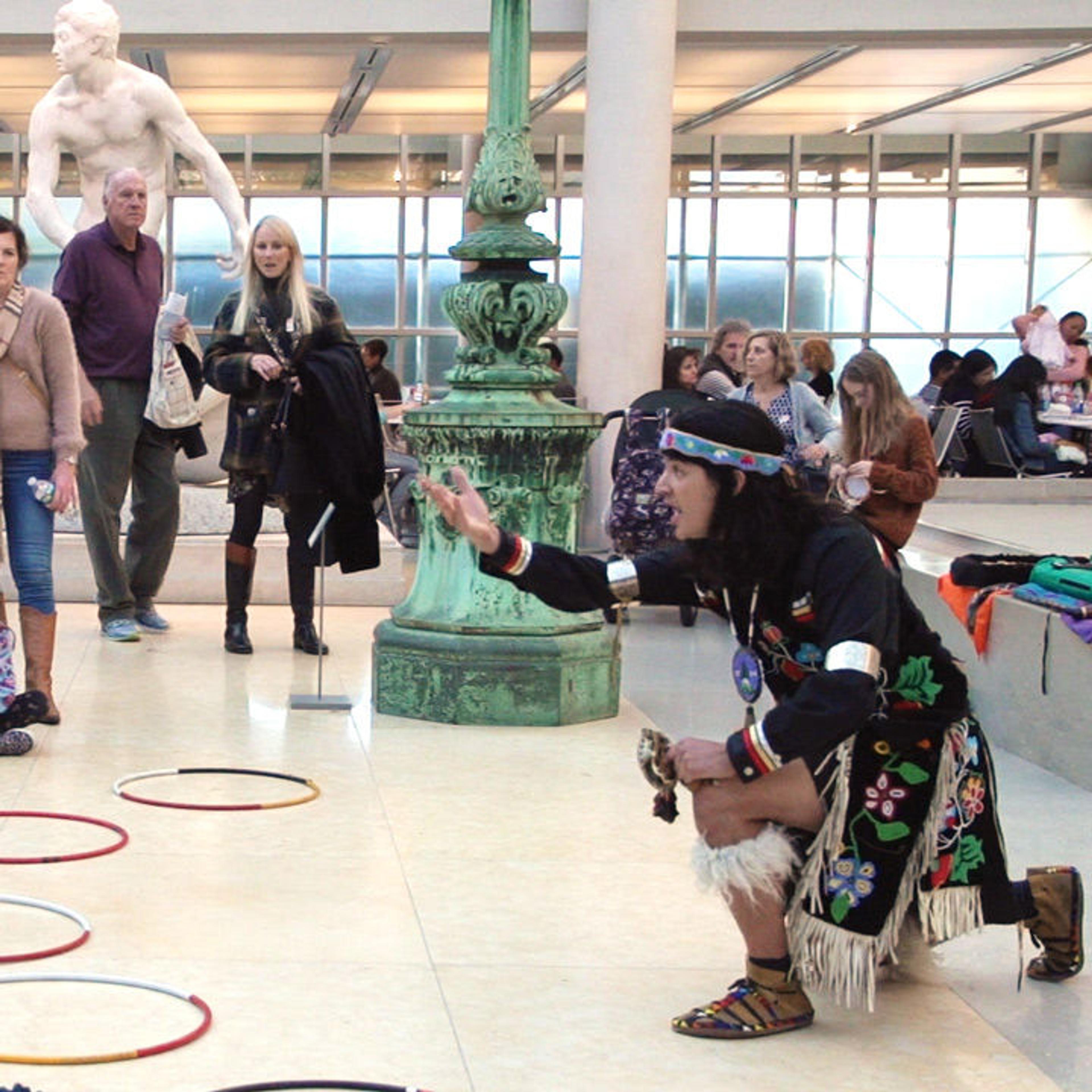 Artist Ty Defoe tells a story to kids and families at The Met. He kneels at the center of a ring of colorful hoops.
