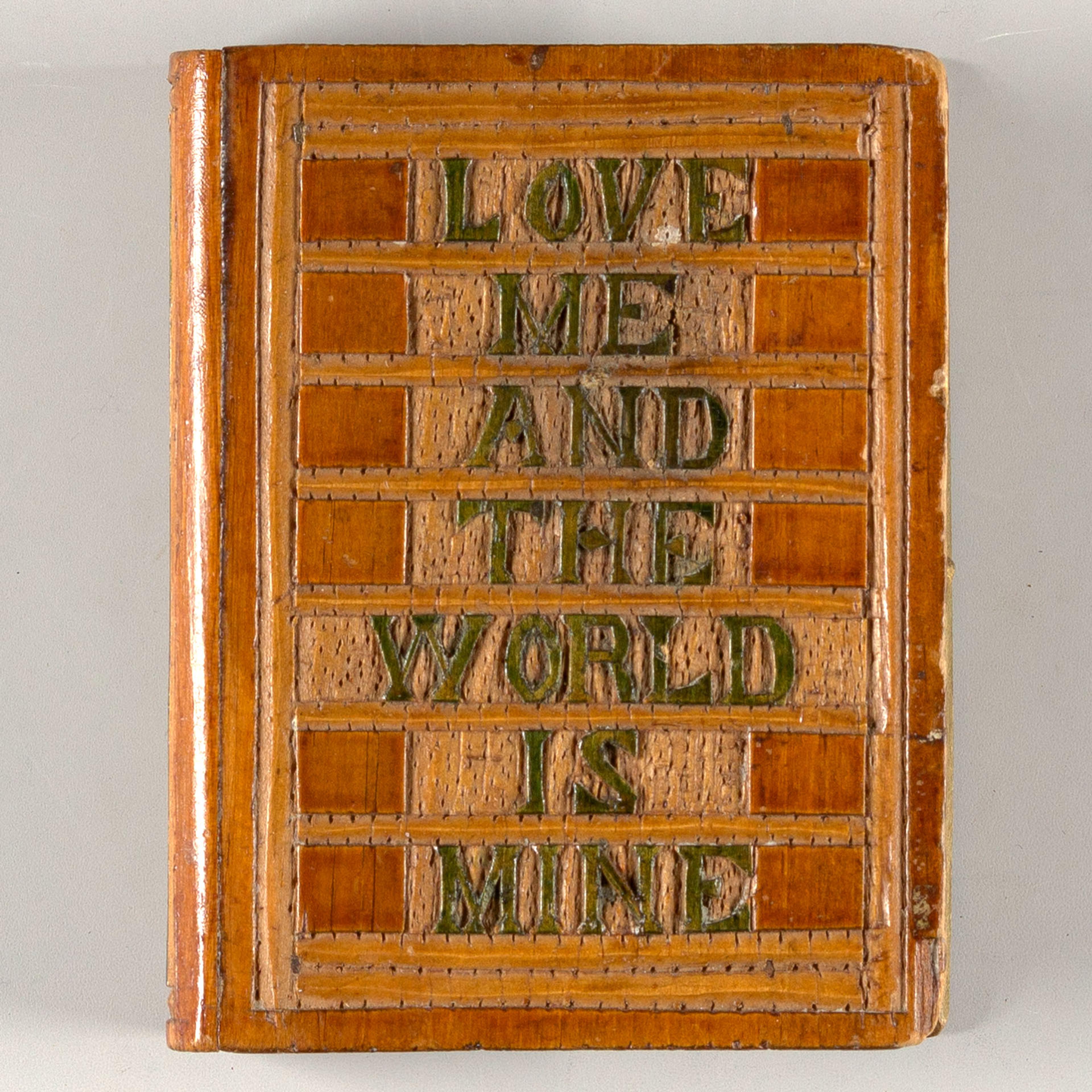 An antique wooden book cover, intricately crafted with a raised lettering message "love me and the world is mine," evoking a sense of vintage charm and romantic ideals.