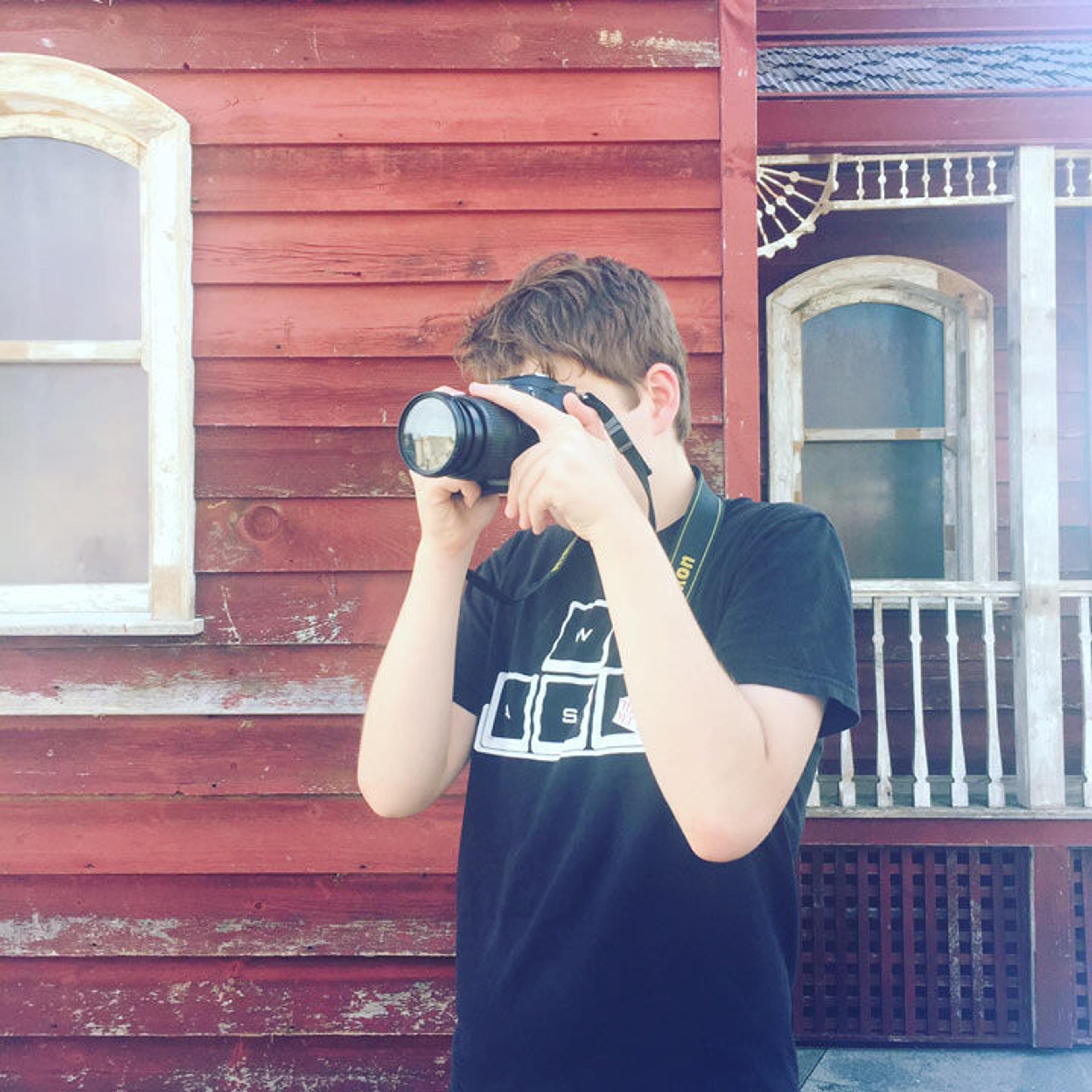 A teen wearing a black shirt takes a photograph in front of a red barn