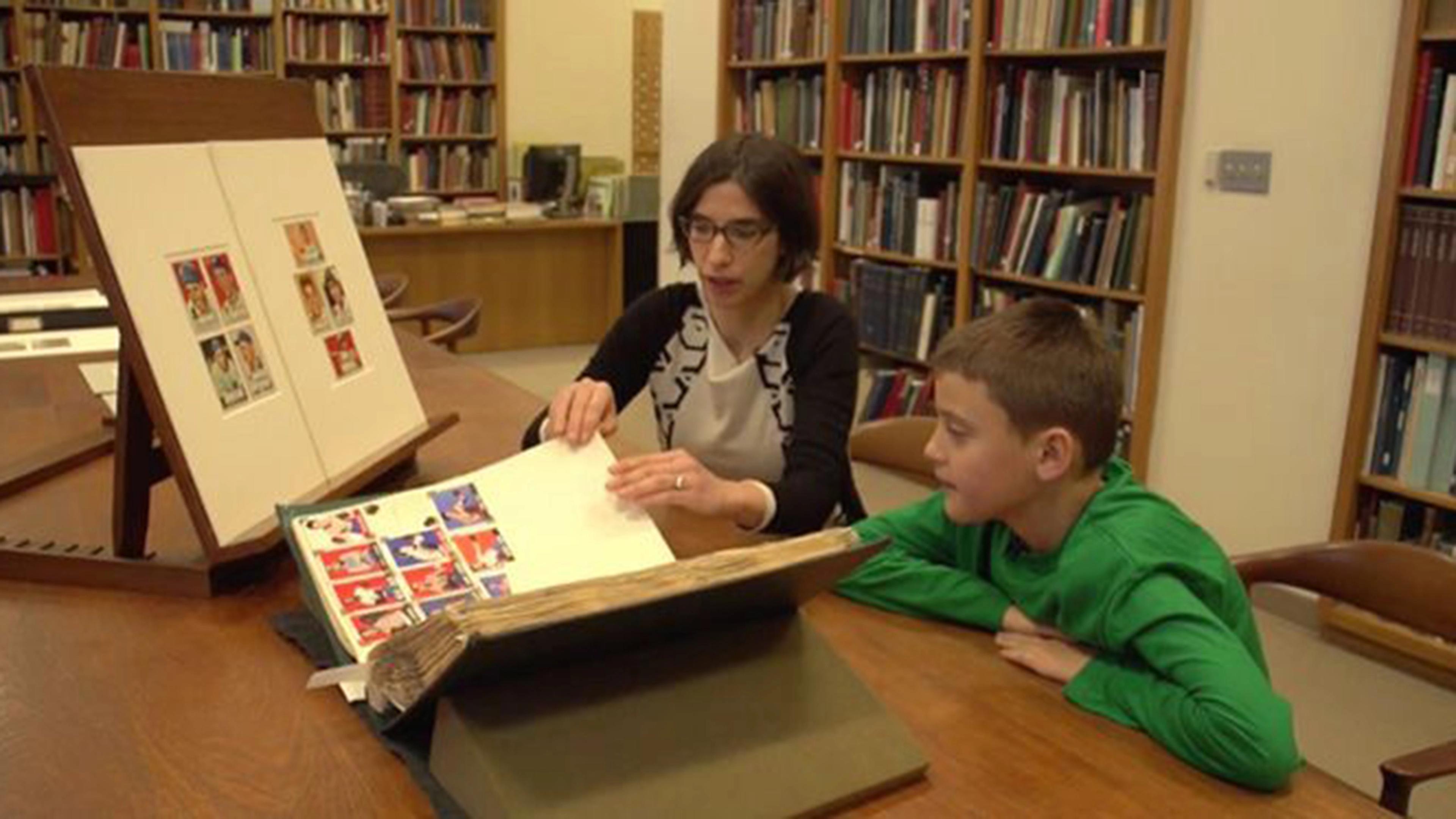 A woman and a child sit at a desk holding displays of sports cards
