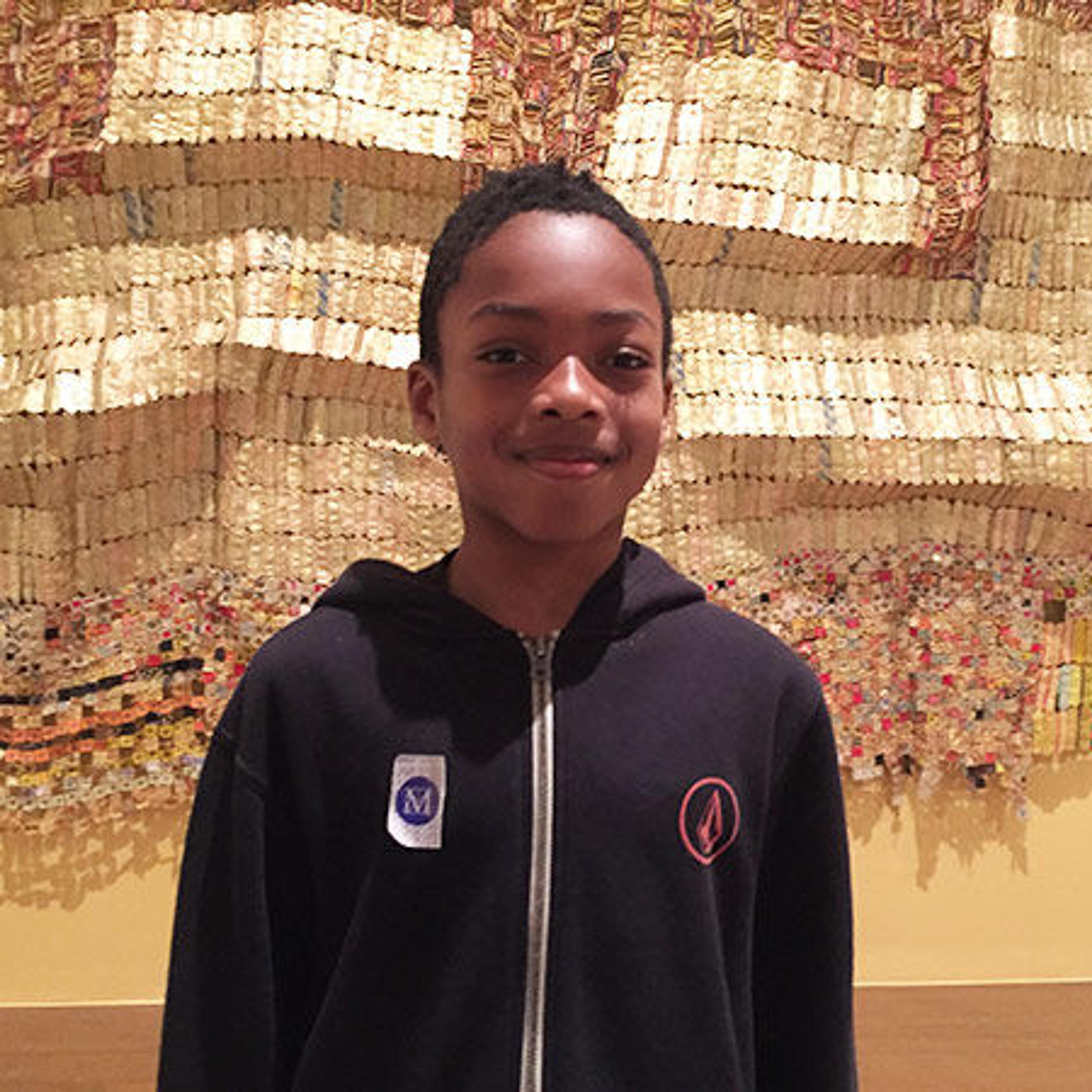 Child smiling in front of an undulating gold artwork.
